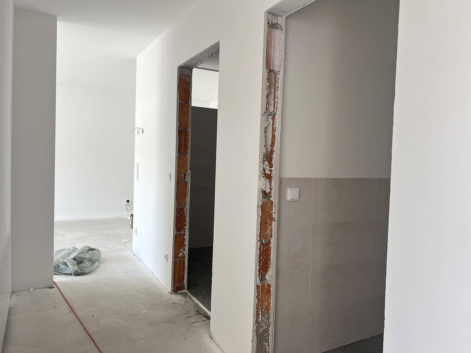 Heller Flur in einem Neubau mit unverputzten Türrahmen und teilgefliesten Wänden.