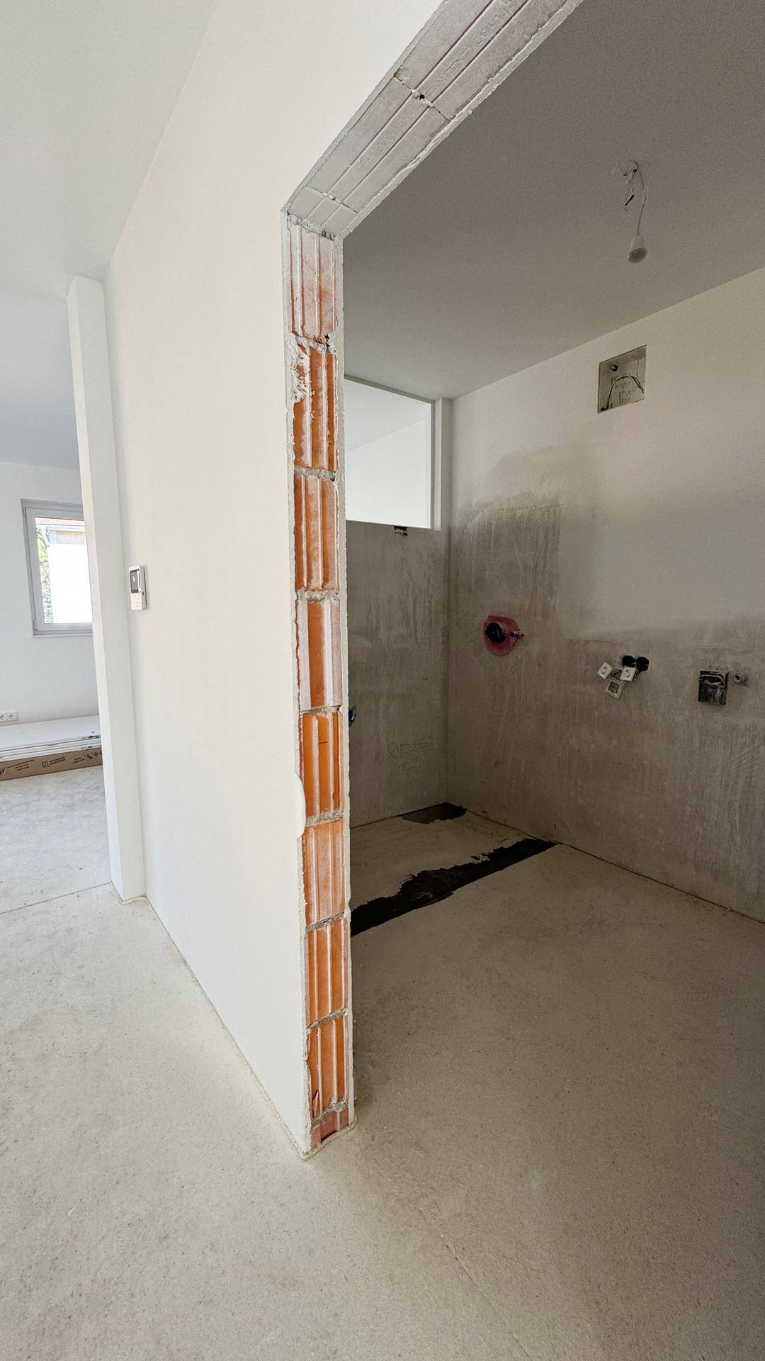 Badezimmer im Rohbau mit Betonboden und sichtbaren Installationen, bereit für die Endmontage.