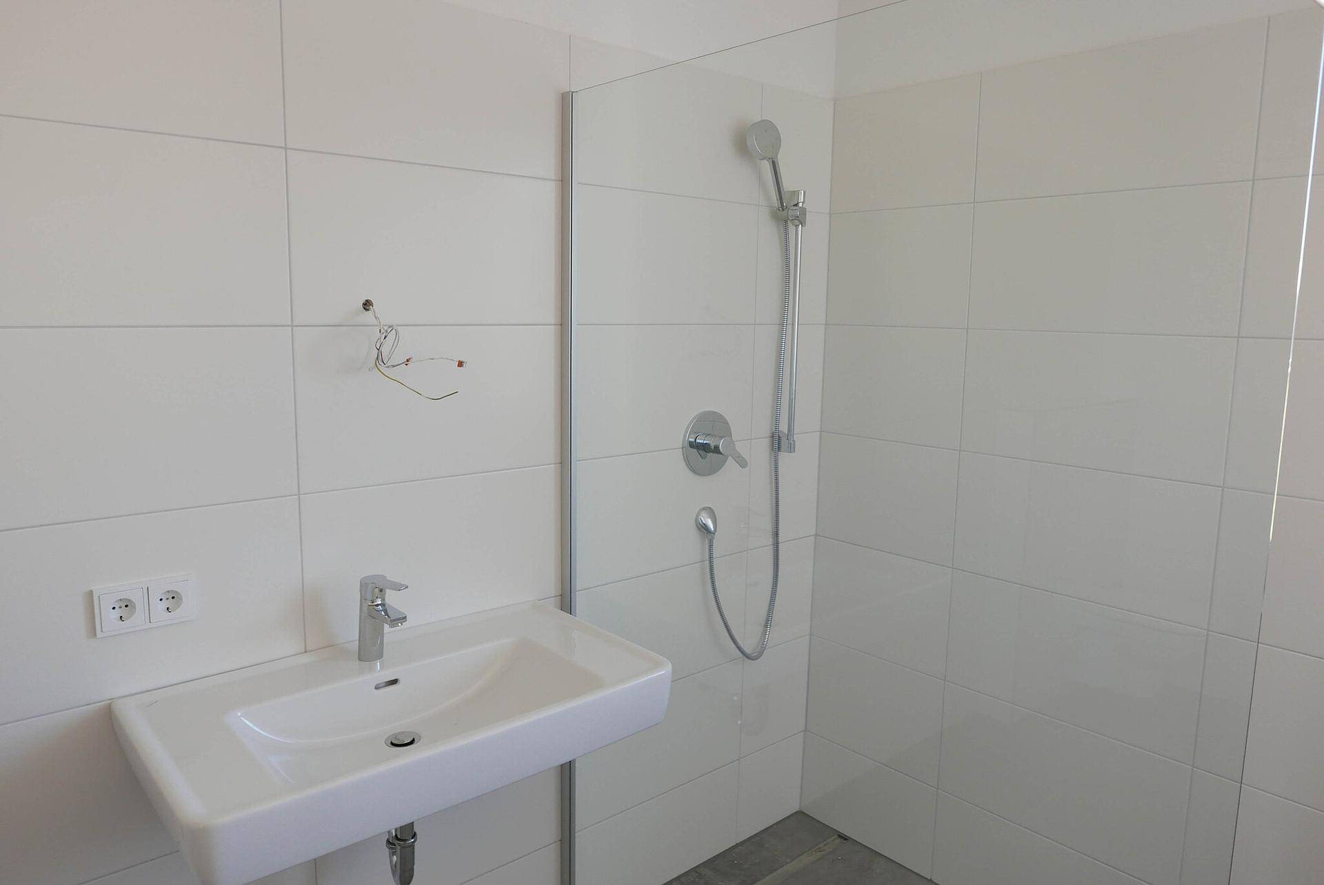 Helles Badezimmer mit Waschbecken und Duschbereich, ausgestattet mit modernen Armaturen.