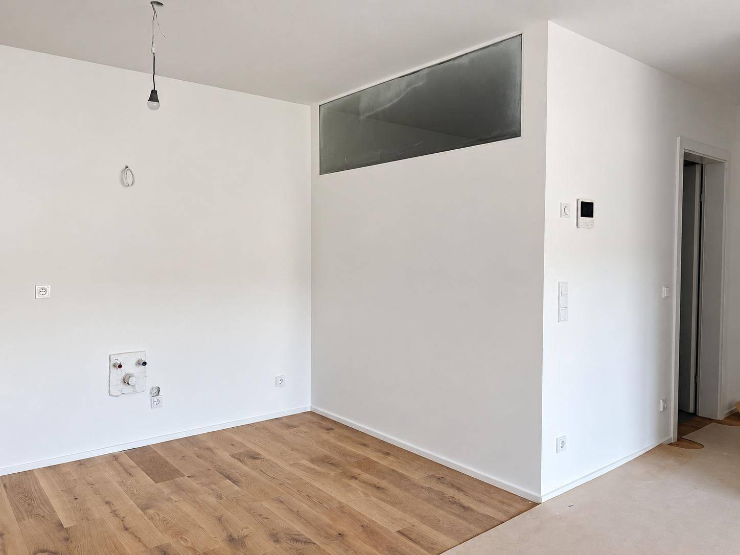 Heller Raum mit vorbereiteten Anschlüssen für eine Küche und Holzboden.