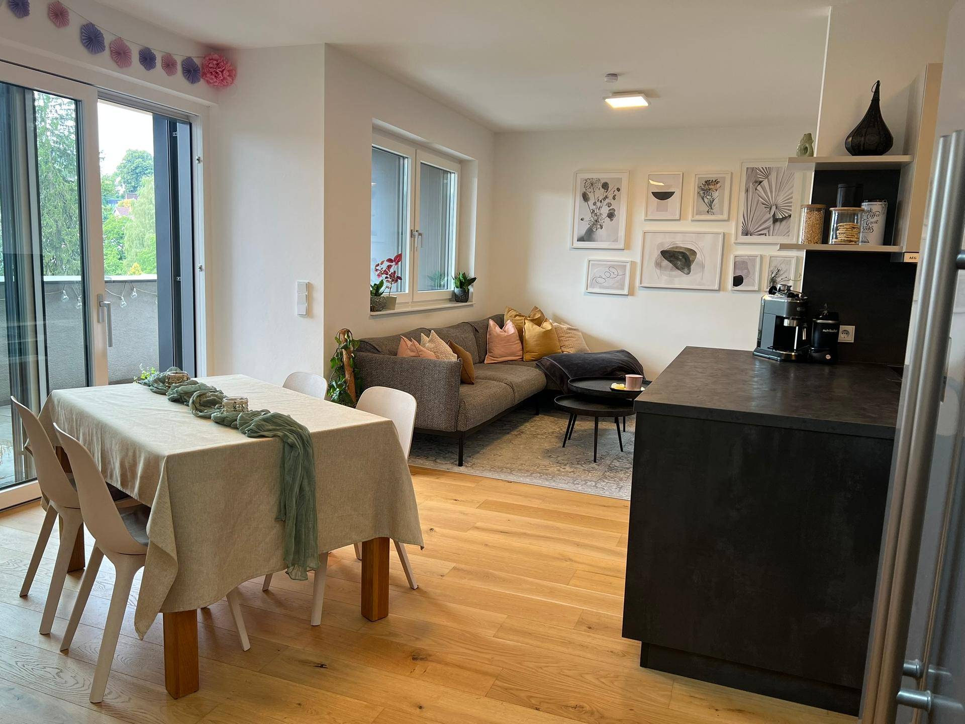 Heller Wohn-Essbereich mit Holzboden, Esstisch und Zugang zum Balkon, offen zur Küche.