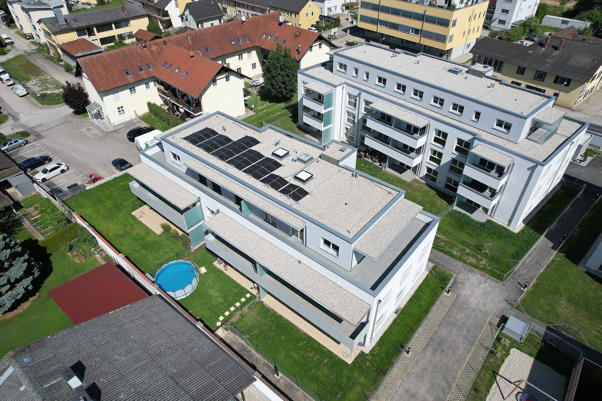 Luftaufnahme einer modernen Wohnanlage mit Flachdächern und Photovoltaikanlagen in städtischer Umgebung.