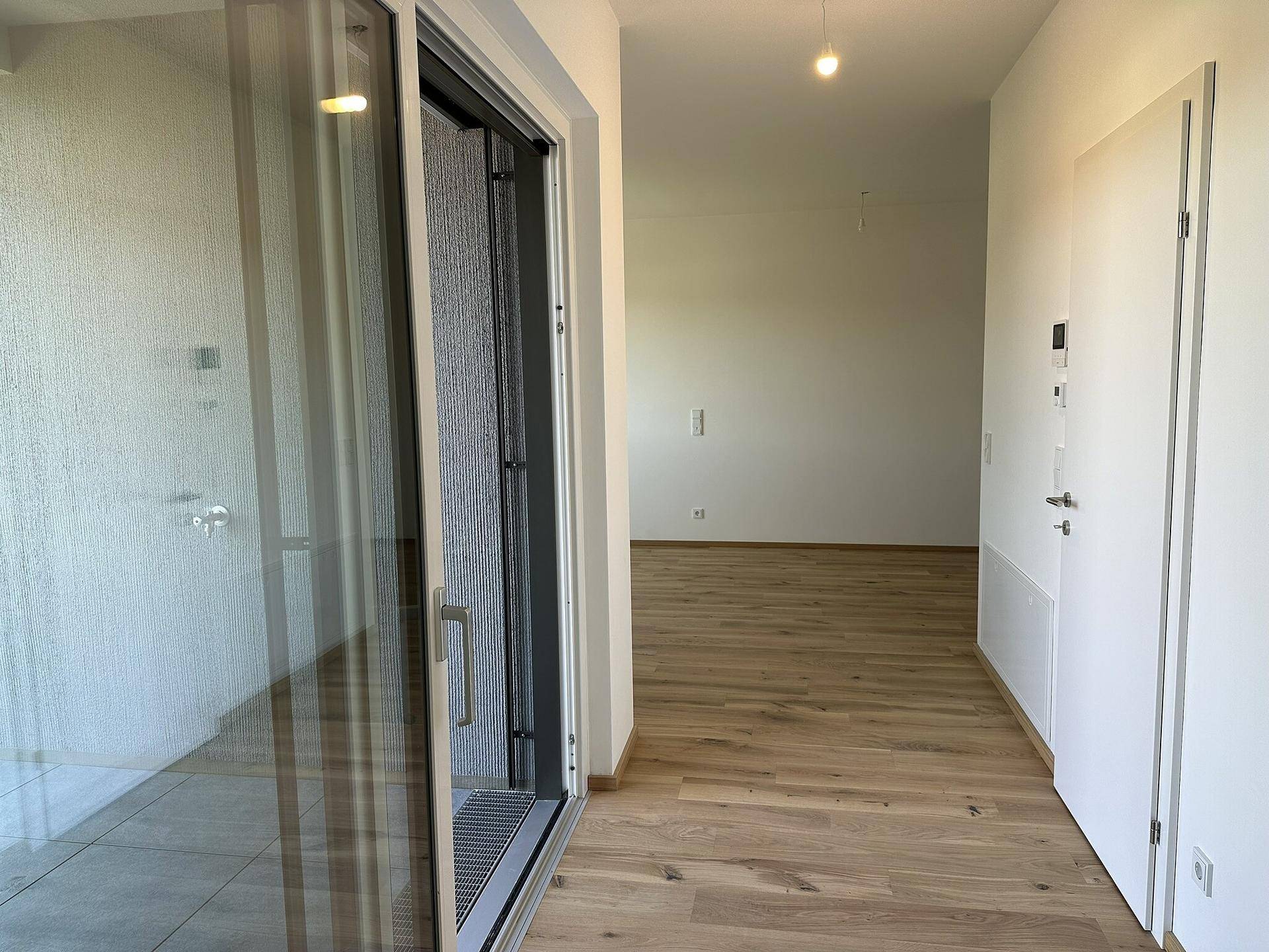 Eingangsbereich mit Holzboden und Zugang zu den Wohnräumen sowie einem hellen Balkon.
