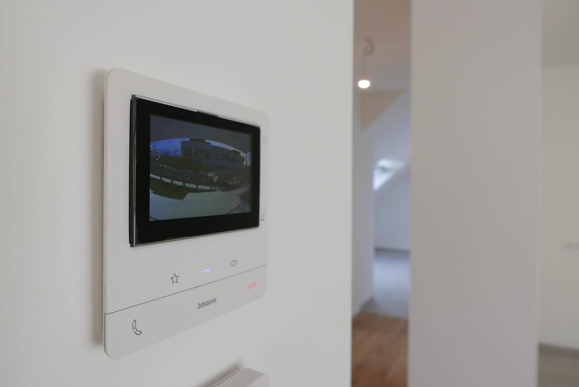 Moderne Video-Gegensprechanlage an einer weißen Wand im Eingangsbereich.