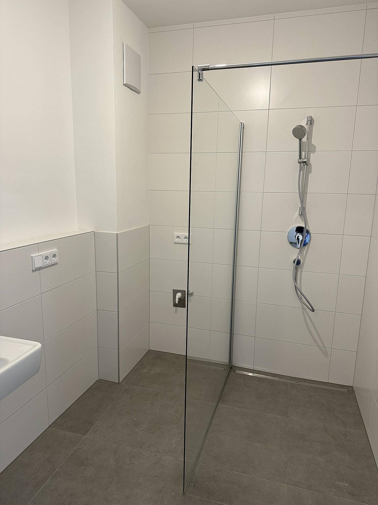 Modernes Badezimmer mit ebenerdiger Dusche, Glasabtrennung und weißen Fliesen an Wänden und Boden.