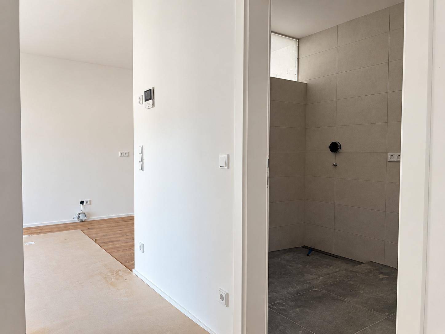Badezimmer im Bau mit hellgrauen Fliesen und einem kleinen Fenster für Tageslicht.