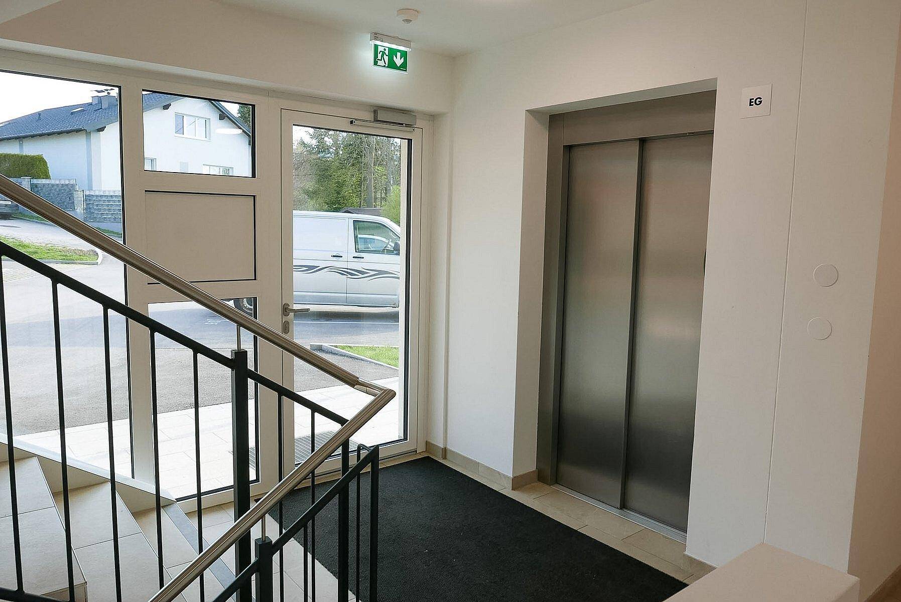 Heller Eingangsbereich mit Treppe und Aufzug, der den Zugang zu den Wohnungen ermöglicht.