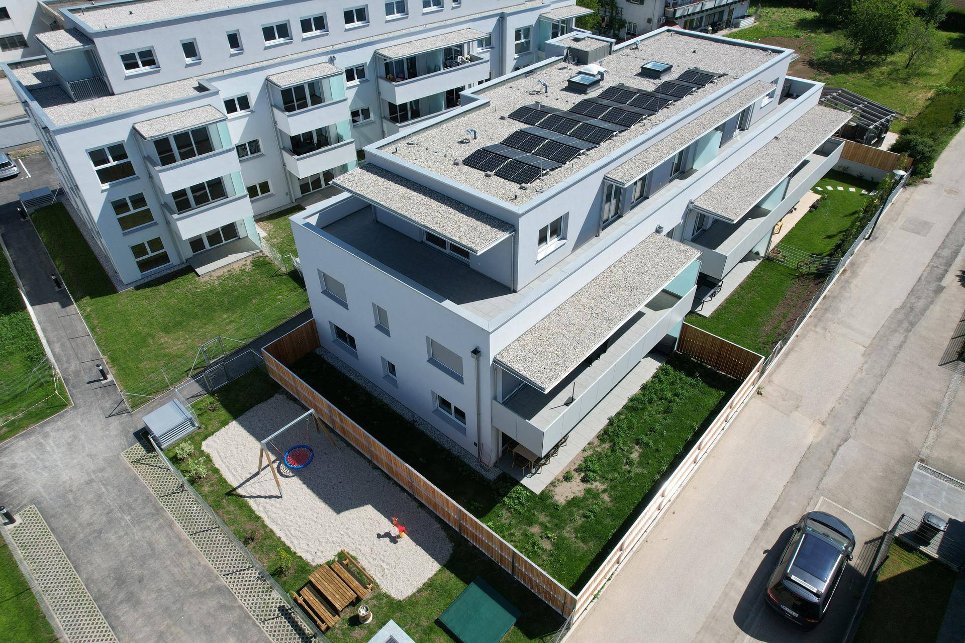 Luftaufnahme einer modernen Wohnanlage mit Flachdächern, Solaranlagen und Gemeinschaftsgrünflächen.