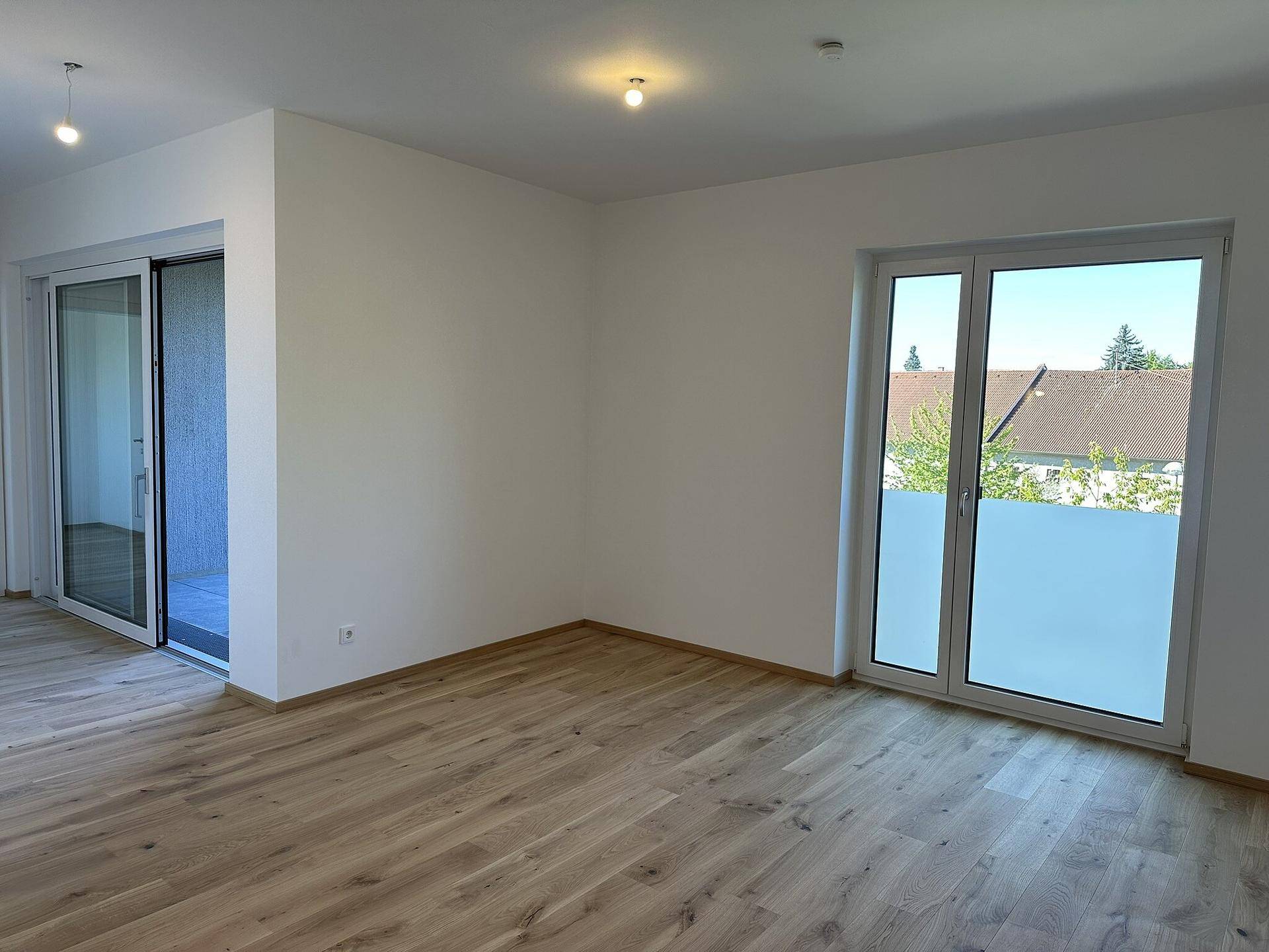 Geräumiger, heller Wohnraum mit großen Fenstern und Holzboden, bereit zur individuellen Gestaltung.