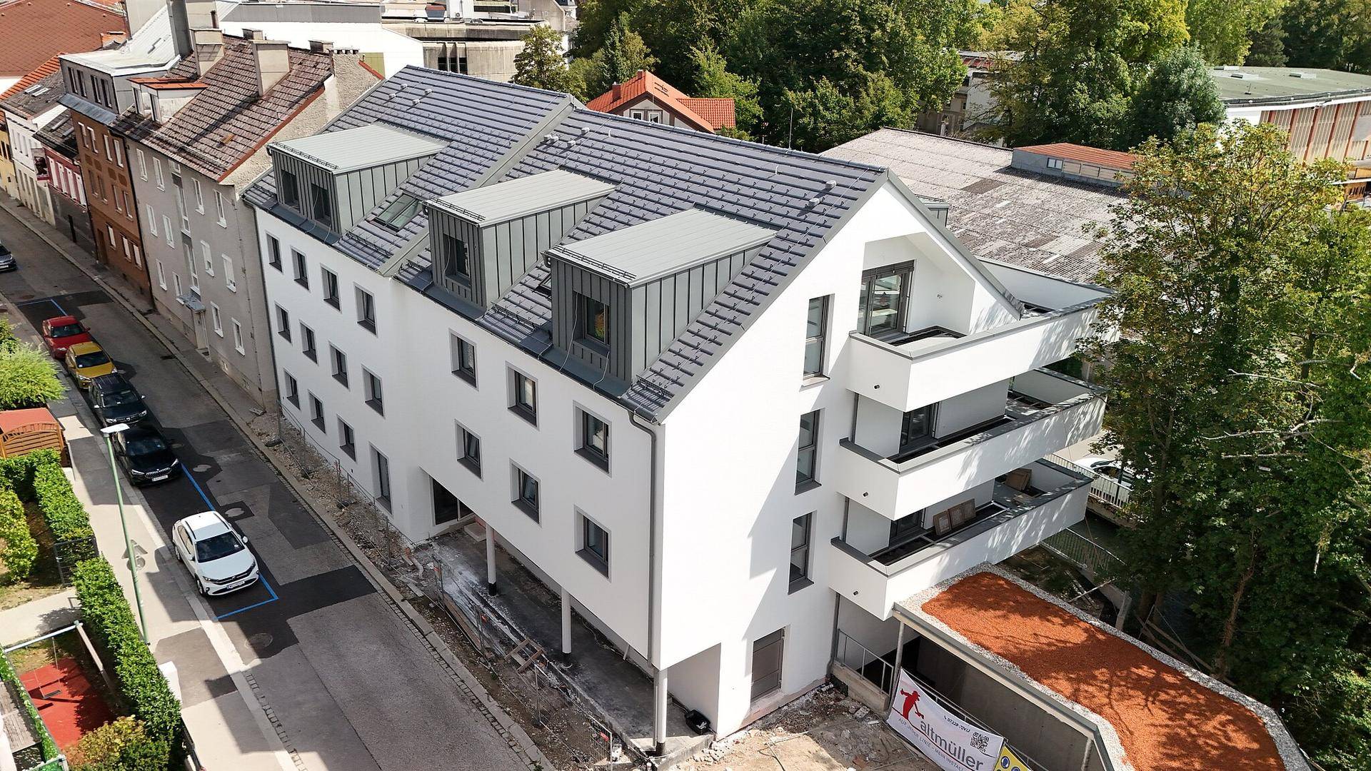Luftaufnahme des Neubaus mit Satteldach, Solaranlagen und Balkonen an der Straßenseite.