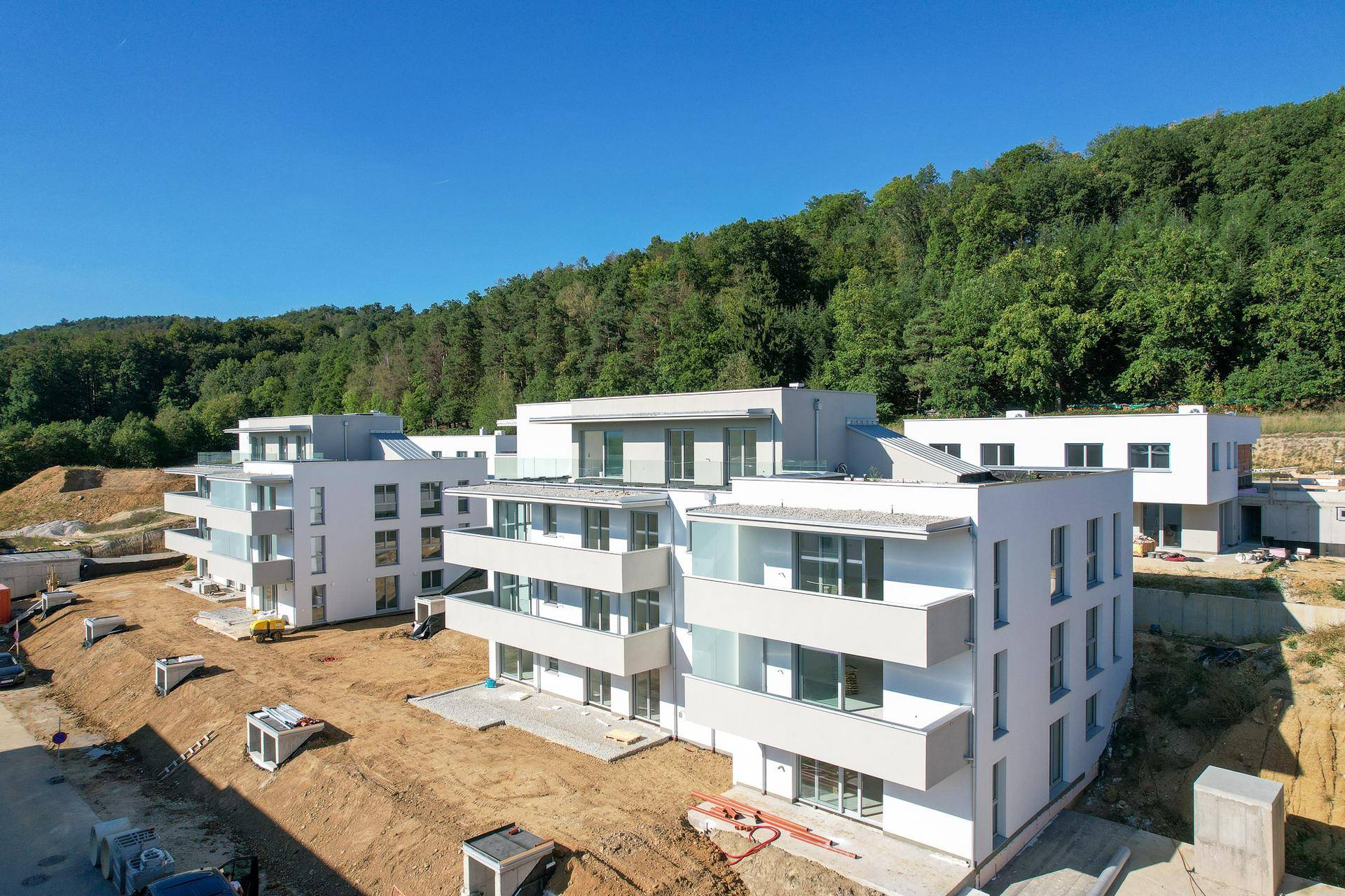 Moderne Wohngebäude im Bau mit Balkonen und großen Fenstern, umgeben von Wald und Natur.