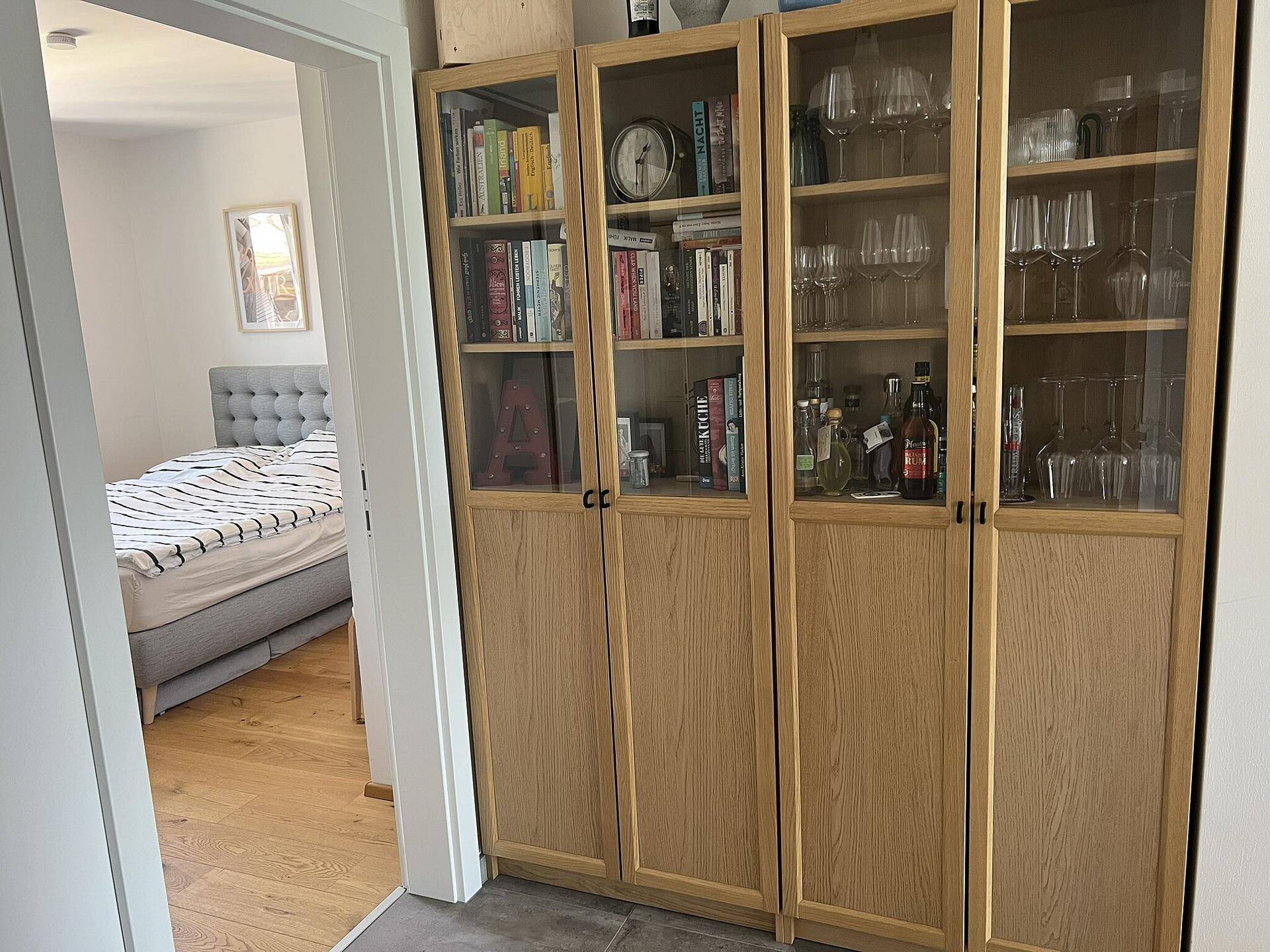 Flur mit Holzregalen und Blick in ein angrenzendes Schlafzimmer mit Doppelbett.