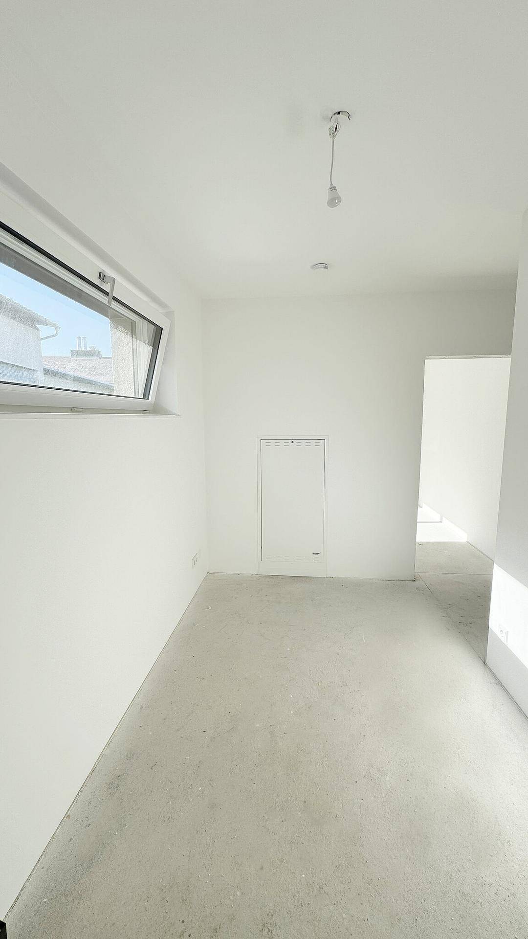 Heller, unmöblierter Raum mit weiß gestrichenen Wänden und einem Fenster, das Tageslicht hereinlässt.