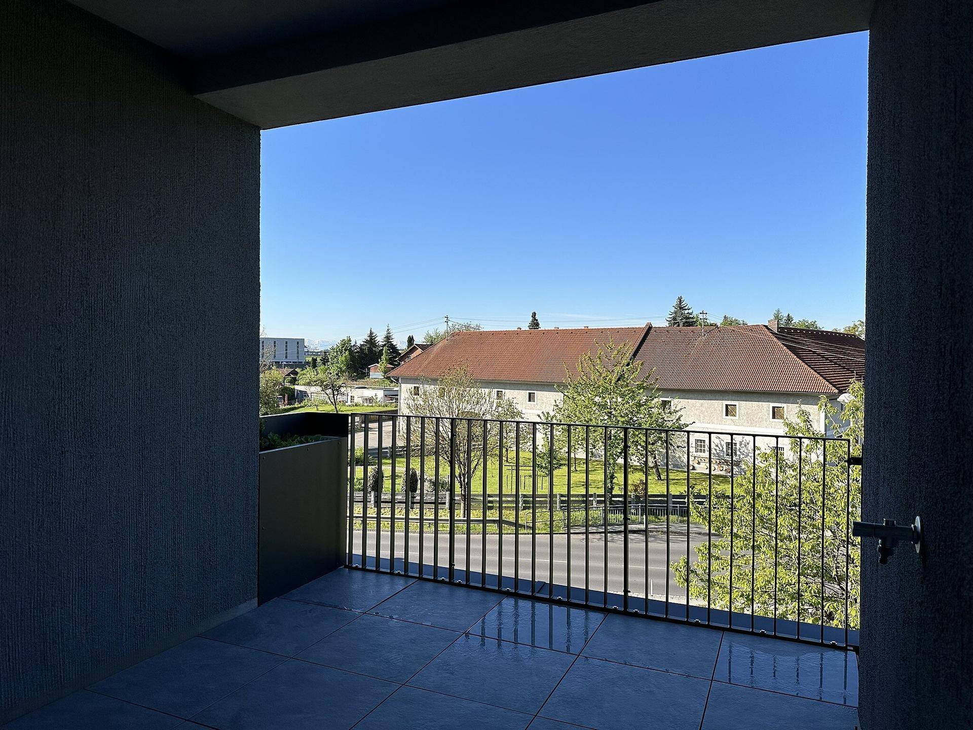 Weitläufiger Balkon mit Metallgeländer und freiem Blick auf die umliegende Landschaft und Häuser.