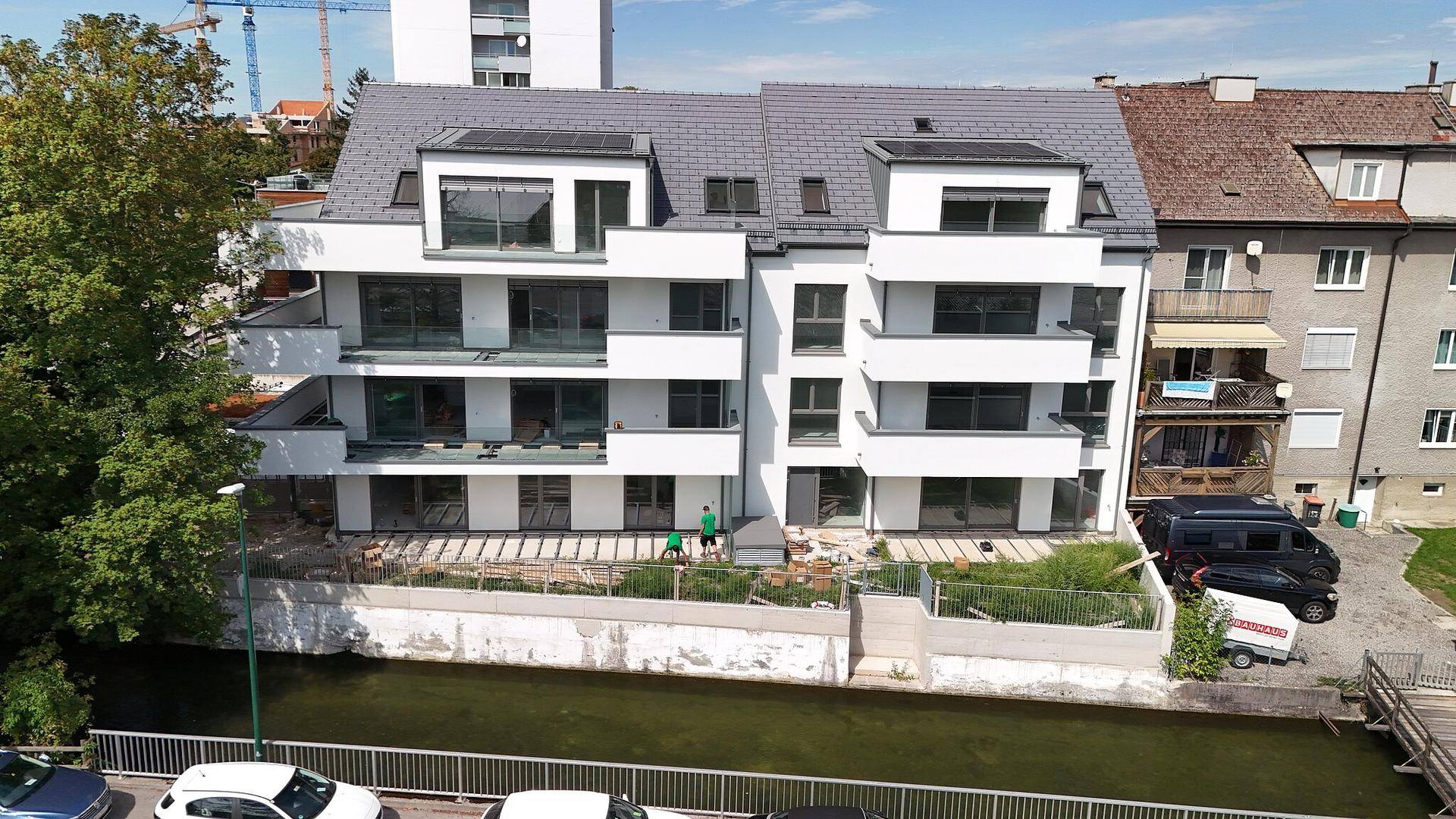 Modernes Wohngebäude mit weißer Fassade, Balkonen und Terrassen am Wasser.