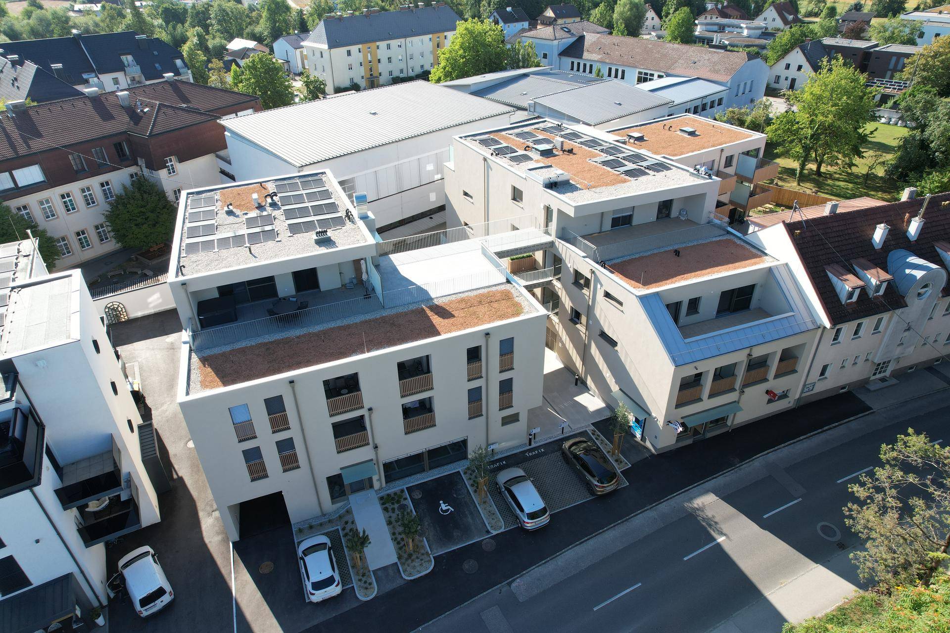 Luftaufnahme eines modernen Wohnkomplexes mit Flachdächern und Photovoltaikanlagen in einer städtischen Umgebung.