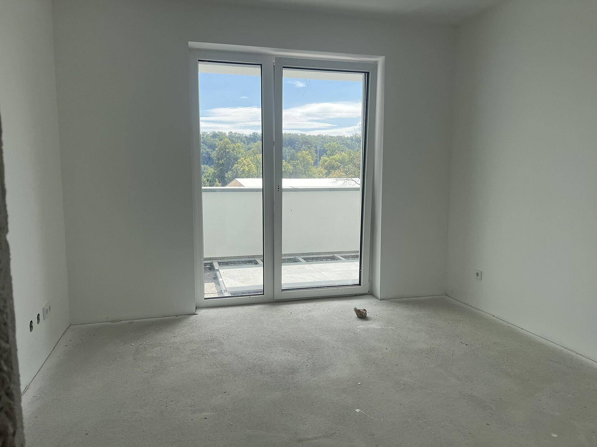 Leerer Raum mit Zugang zu einem Balkon, großen Fenstern und viel natürlichem Licht.