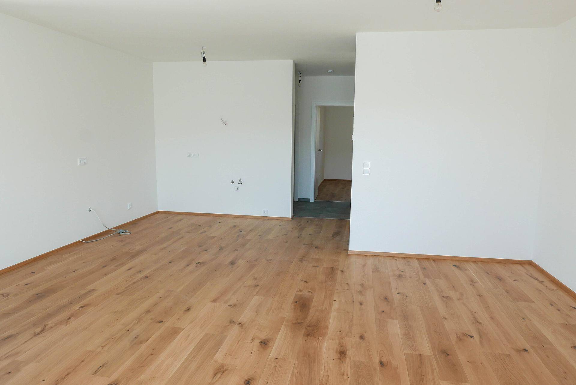 Geräumiges, leeres Wohnzimmer mit Holzboden und Zugang zu weiteren Räumen.