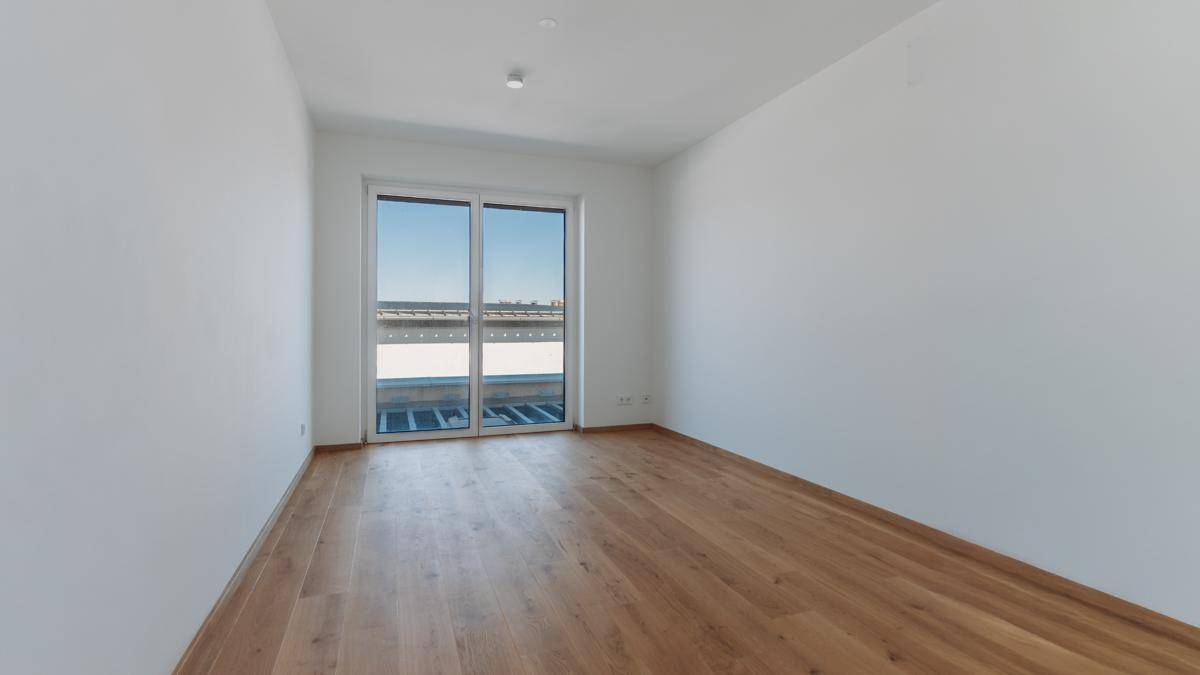 Helles, leeres Zimmer mit Holzboden und großer Schiebetür, die zu einem Außenbereich führt.