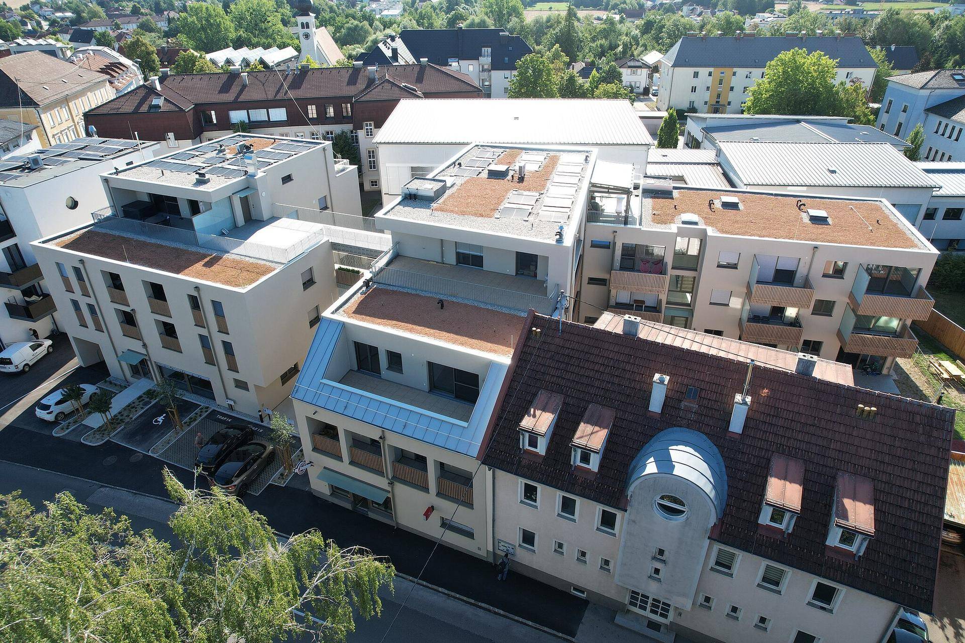 Luftaufnahme eines Wohnkomplexes mit modernen Gebäuden und traditionellen Dächern in einer städtischen Umgebung.