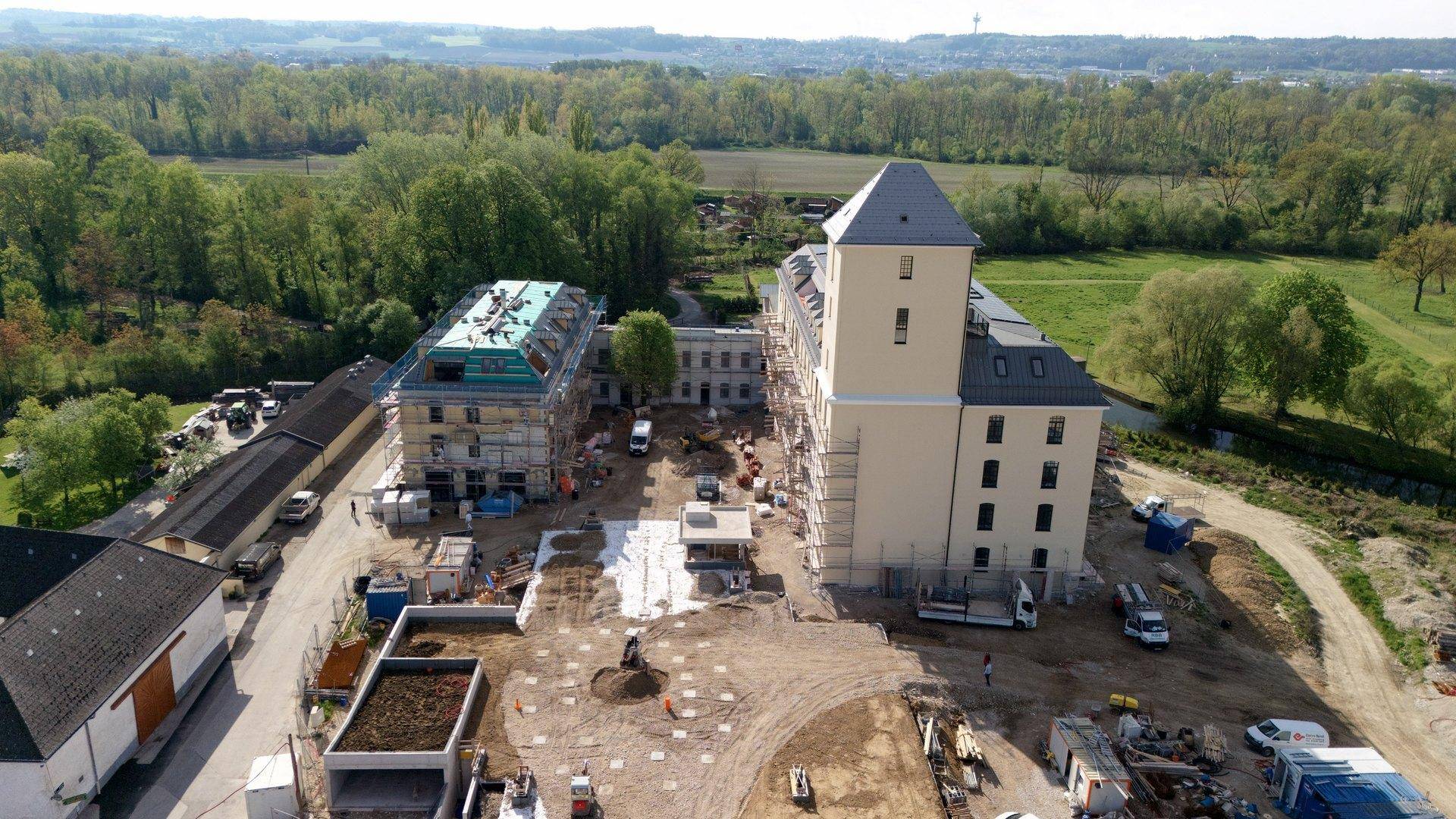 Luftaufnahme einer Baustelle mit mehreren Gebäuden und umliegenden Grünflächen.