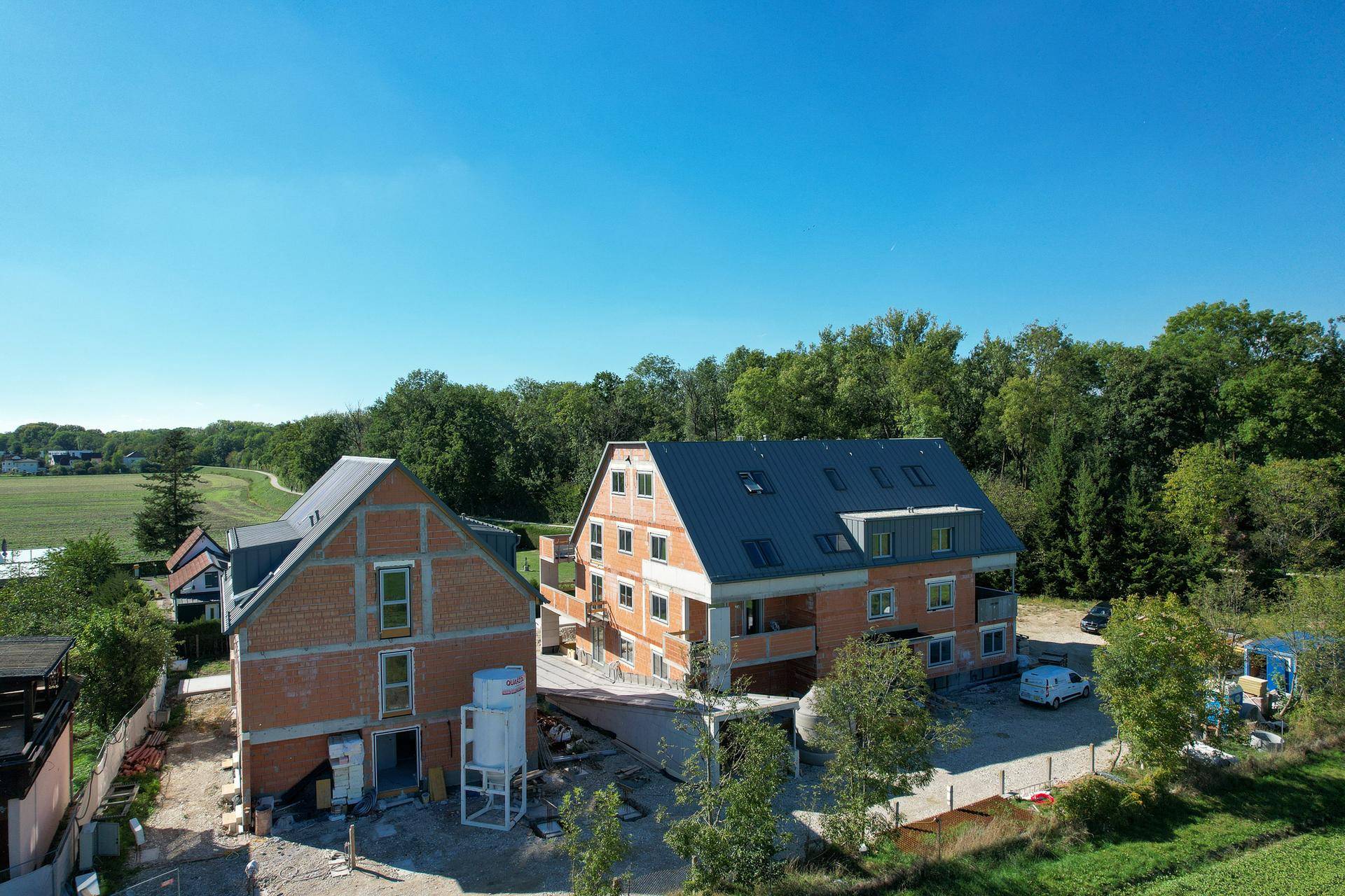 Luftaufnahme von zwei Neubauten im Rohbau, umgeben von Natur und weiten Feldern.