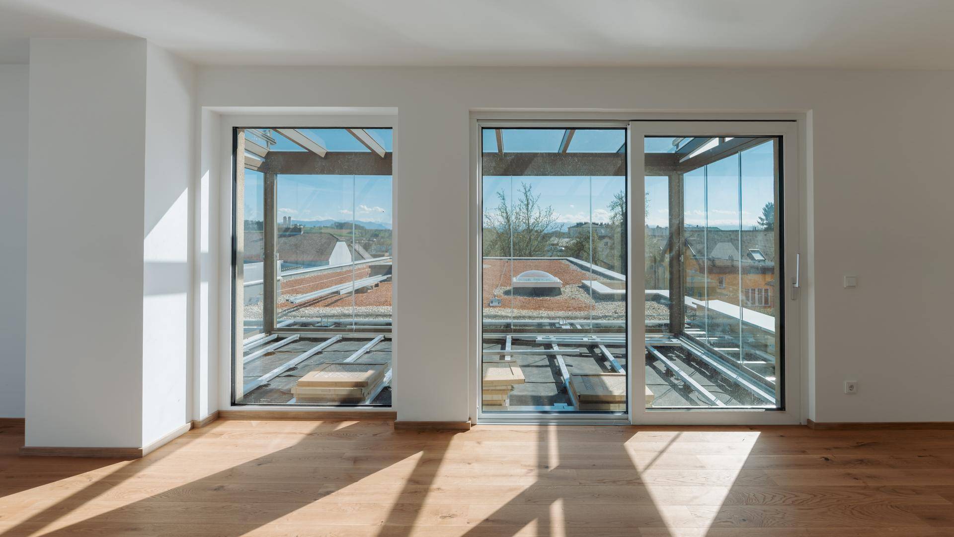 Lichtdurchfluteter Raum mit Holzboden und großen Glasfronten, die einen Blick auf die Umgebung bieten.
