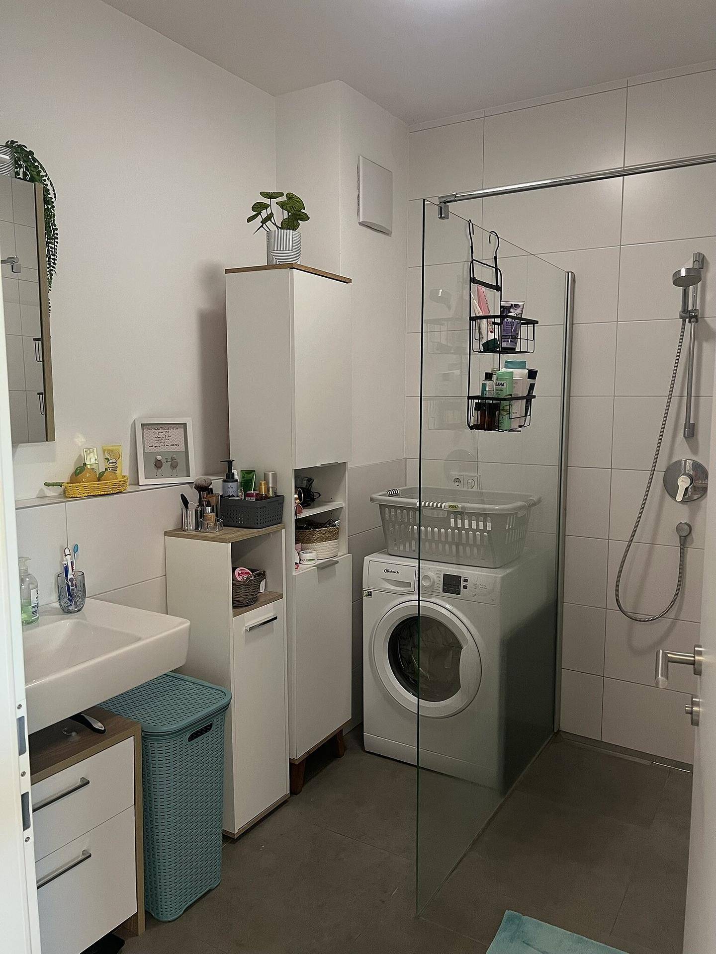 Modernes Badezimmer mit Dusche, Waschmaschine und weißen Fliesen, funktional und hell.