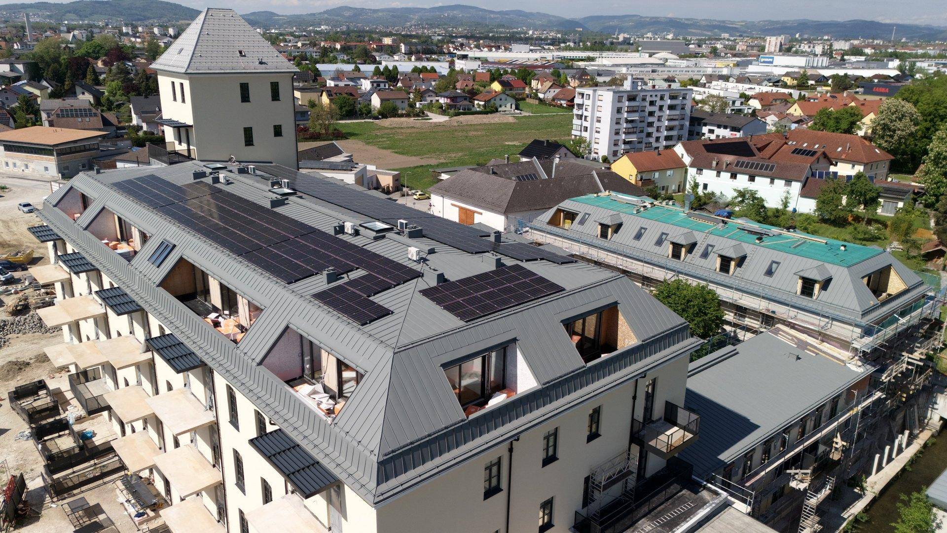 Luftaufnahme eines Neubaus mit Solarmodulen auf dem Dach und Blick auf die Stadt.