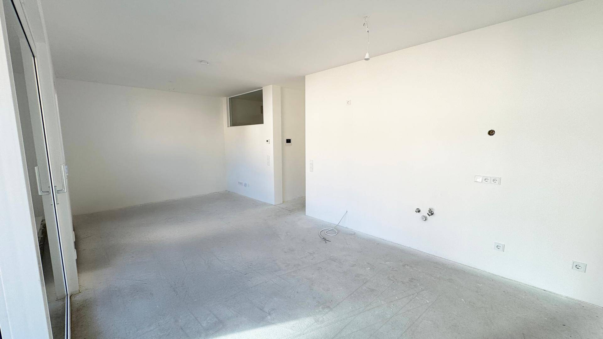 Geräumiger Rohbau mit weißen Wänden, Betonboden und großen Fensteröffnungen, ideal für individuelle Gestaltung.