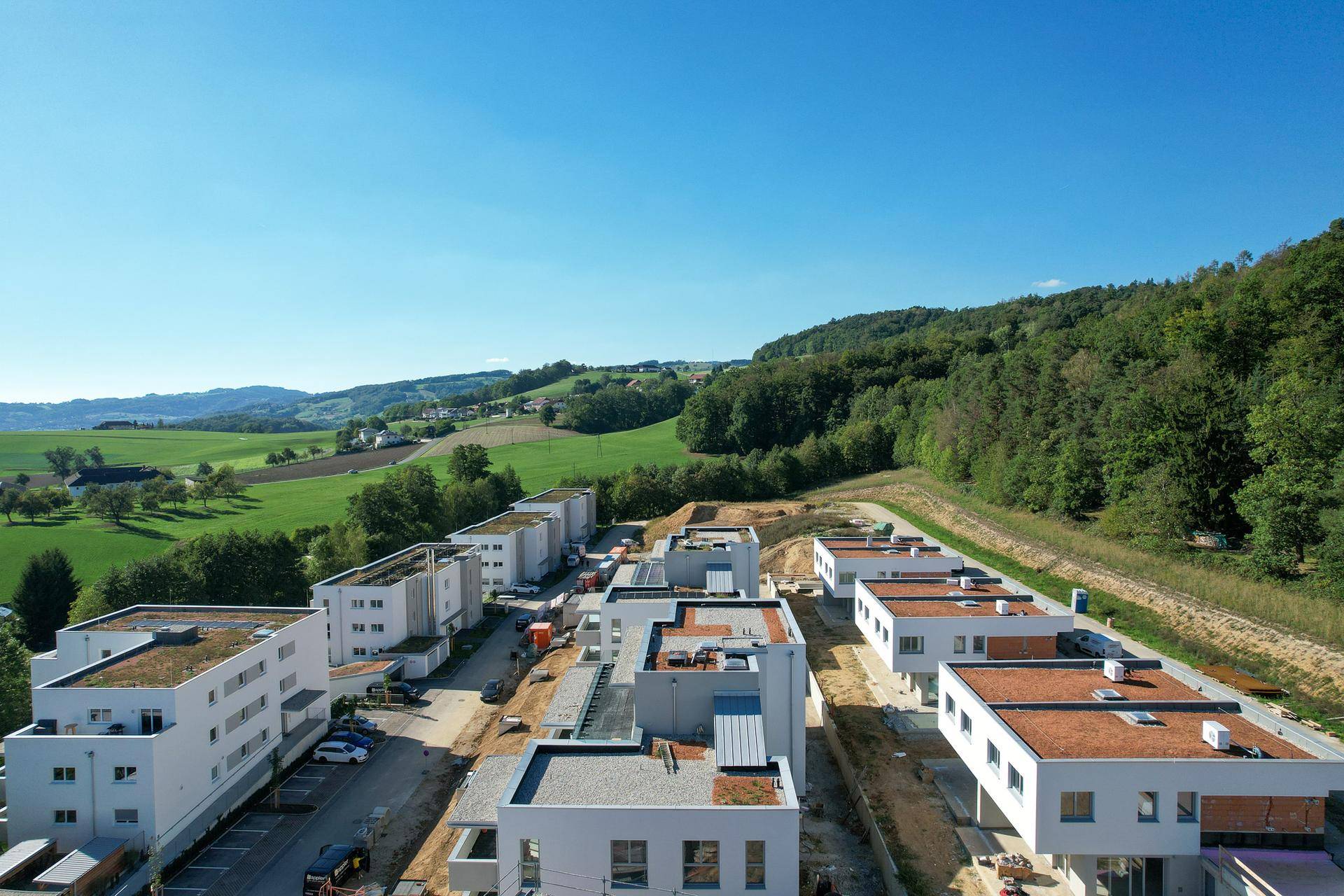 Weitläufige Wohnsiedlung mit modernen Gebäuden und Gründächern, eingebettet in eine ländliche Landschaft.