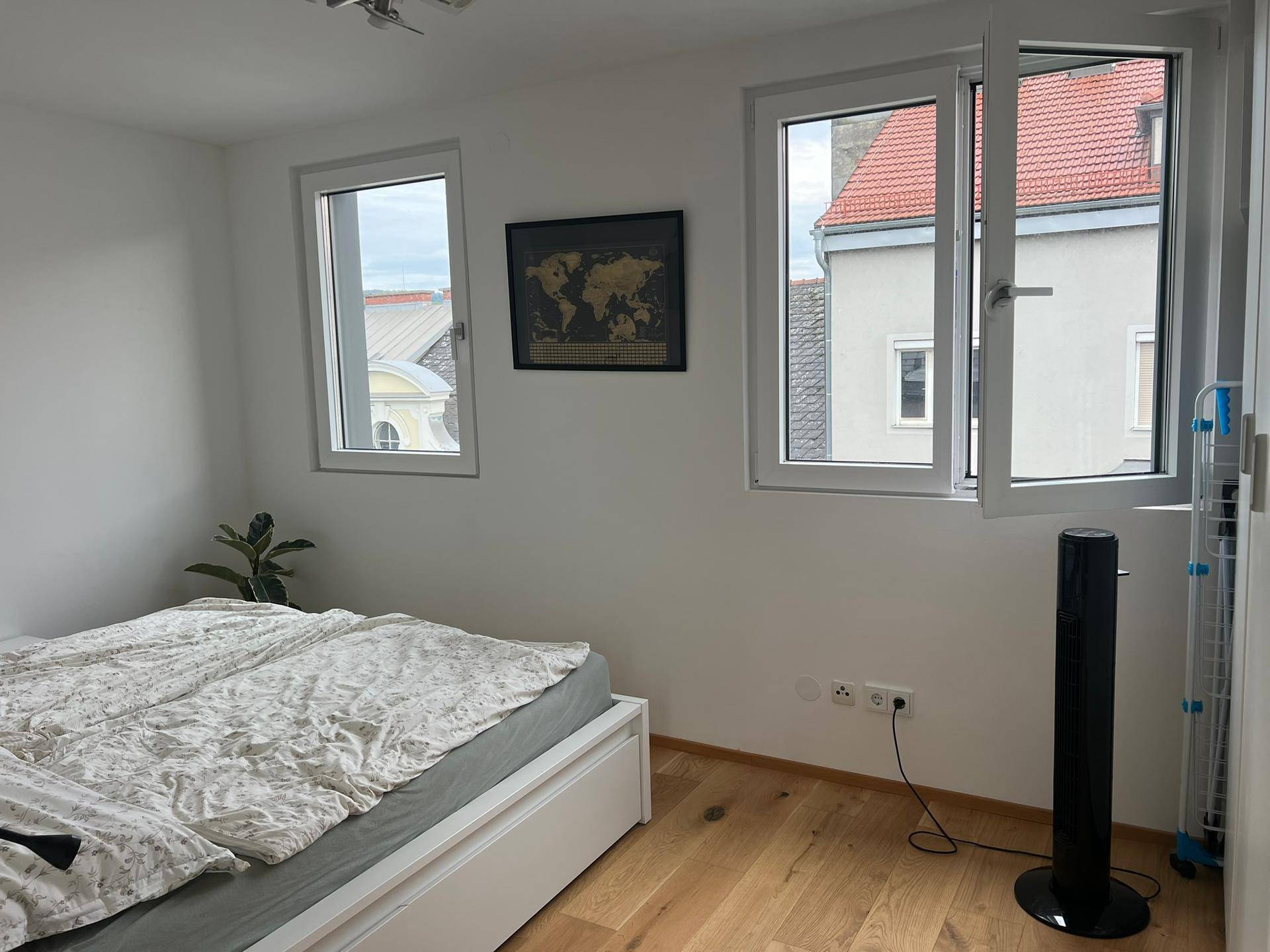 Schlafzimmer mit Doppelbett, Holzboden und zwei Fenstern, die viel Licht hereinlassen.