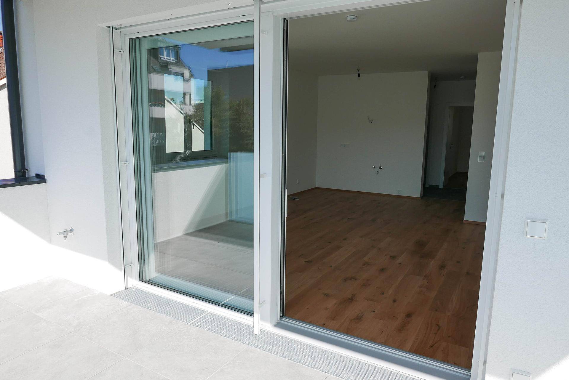 Heller Wohnbereich mit Holzboden und großen Schiebetüren zum Balkon.