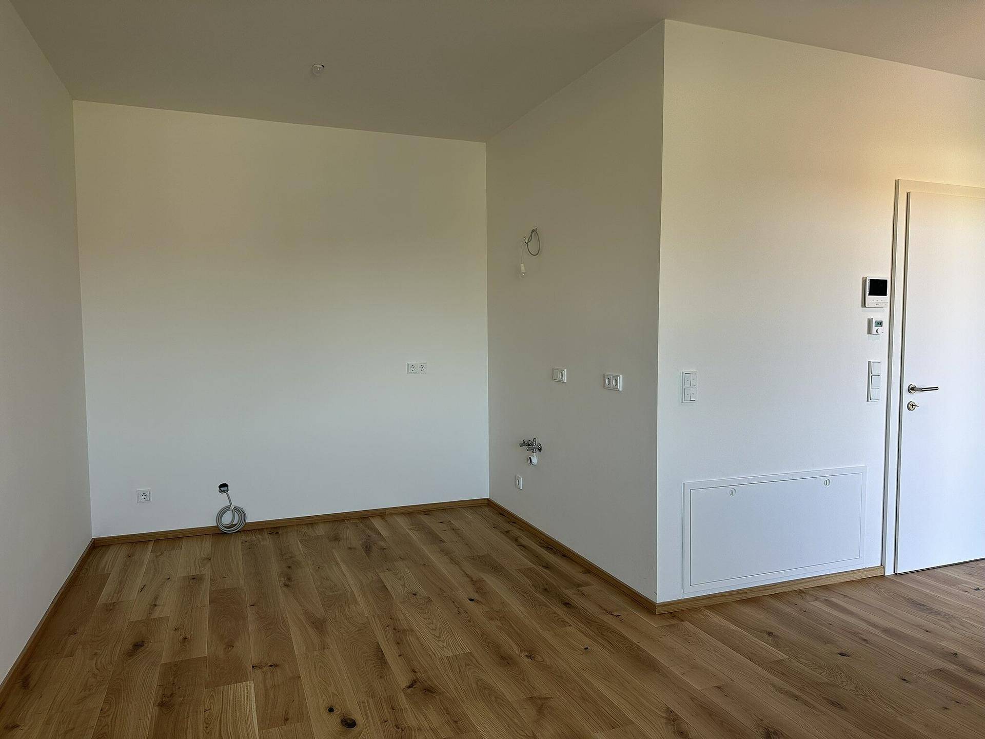 Leerer Raum mit Anschlüssen für eine Küche oder einen Hauswirtschaftsbereich, ausgestattet mit Holzboden.