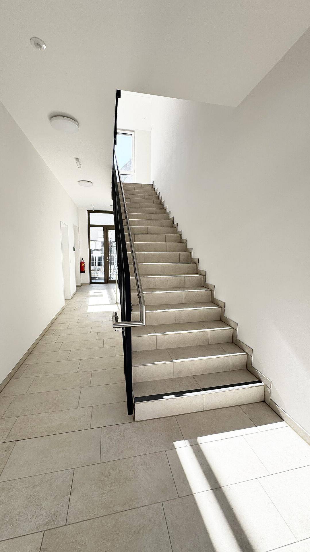 Heller, moderner Treppenaufgang und Flur mit Fliesenboden und viel natürlichem Licht.
