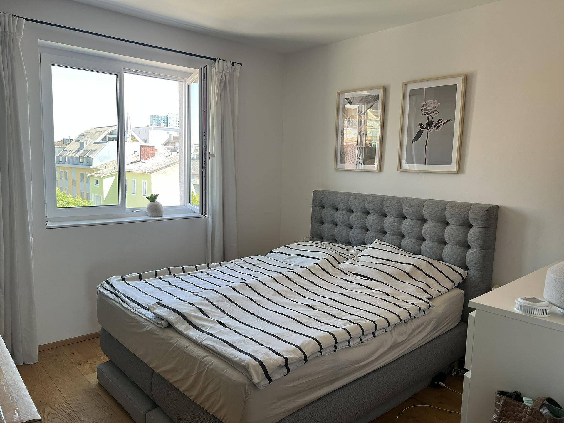 Helles Schlafzimmer mit großem Bett, Holzboden und Fenster mit Stadtblick.