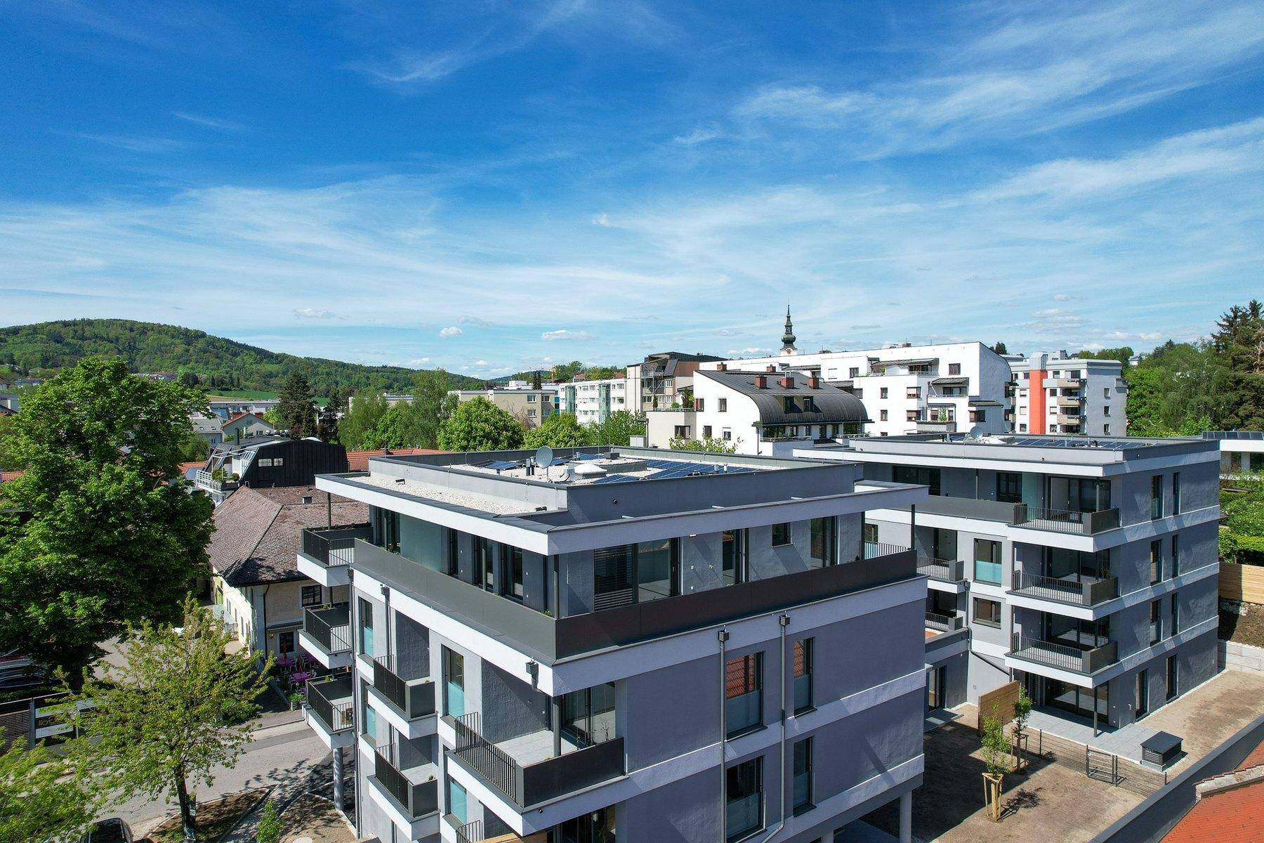 Luftaufnahme eines modernen Wohnkomplexes mit Flachdächern und Stadtblick, umgeben von Grünflächen.