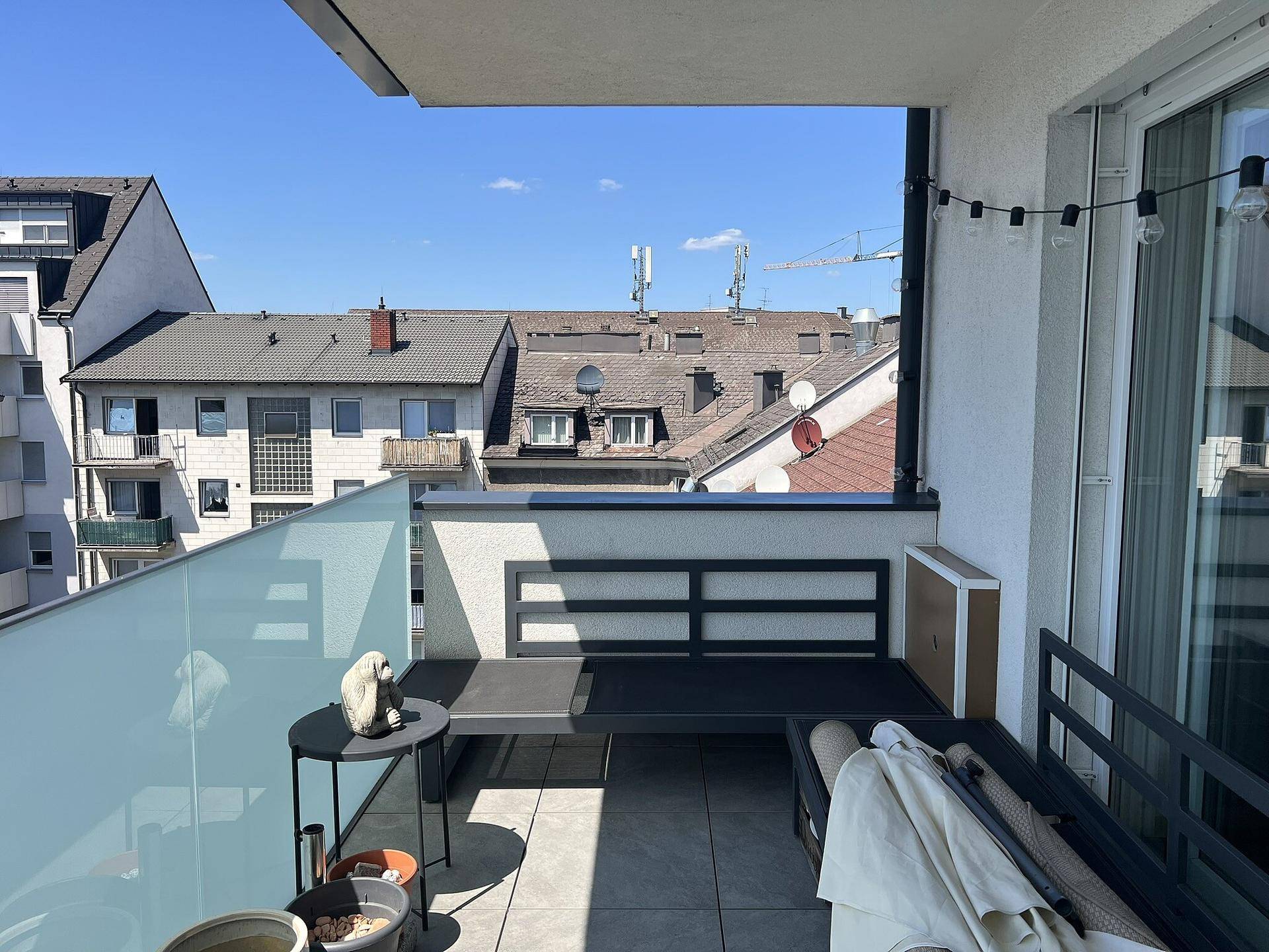 Sonniger Balkon mit moderner Sitzgelegenheit und Blick auf die Dächer der Stadt.