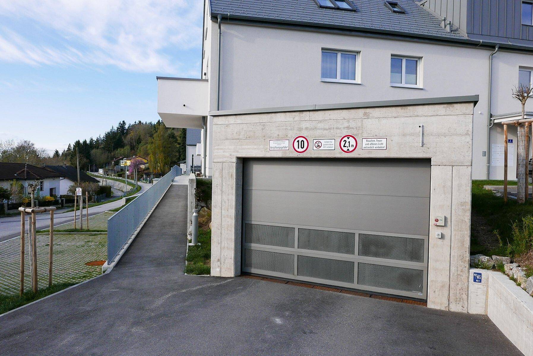 Zufahrt zur Tiefgarage eines modernen Wohngebäudes mit Rampe und Garagentor.