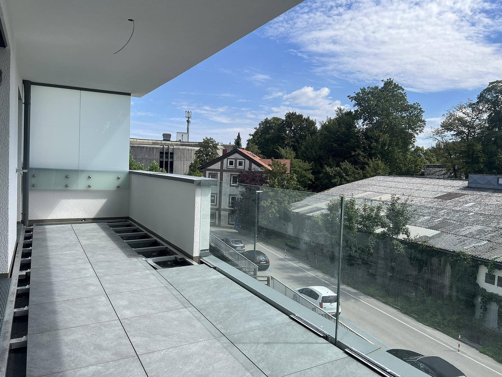 Breiter Balkon mit Glasgeländer und Blick auf die Straße und umliegende Gebäude.