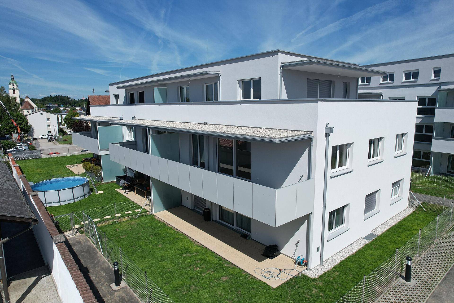 Moderne Wohnanlage mit Flachdach, Balkonen und einem kleinen Gartenbereich mit Aufstellpool.