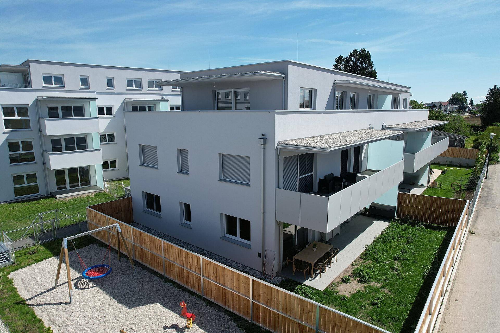 Erdgeschosswohnung mit Terrasse, Gartenmöbeln und angrenzendem Kinderspielplatz.