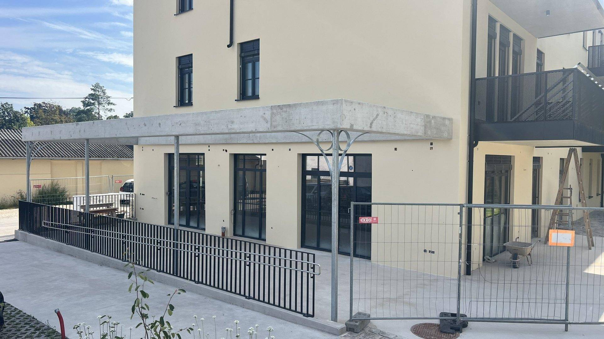 Gebäudeeingang mit einer barrierefreien Rampe und einem Vordach aus Beton.