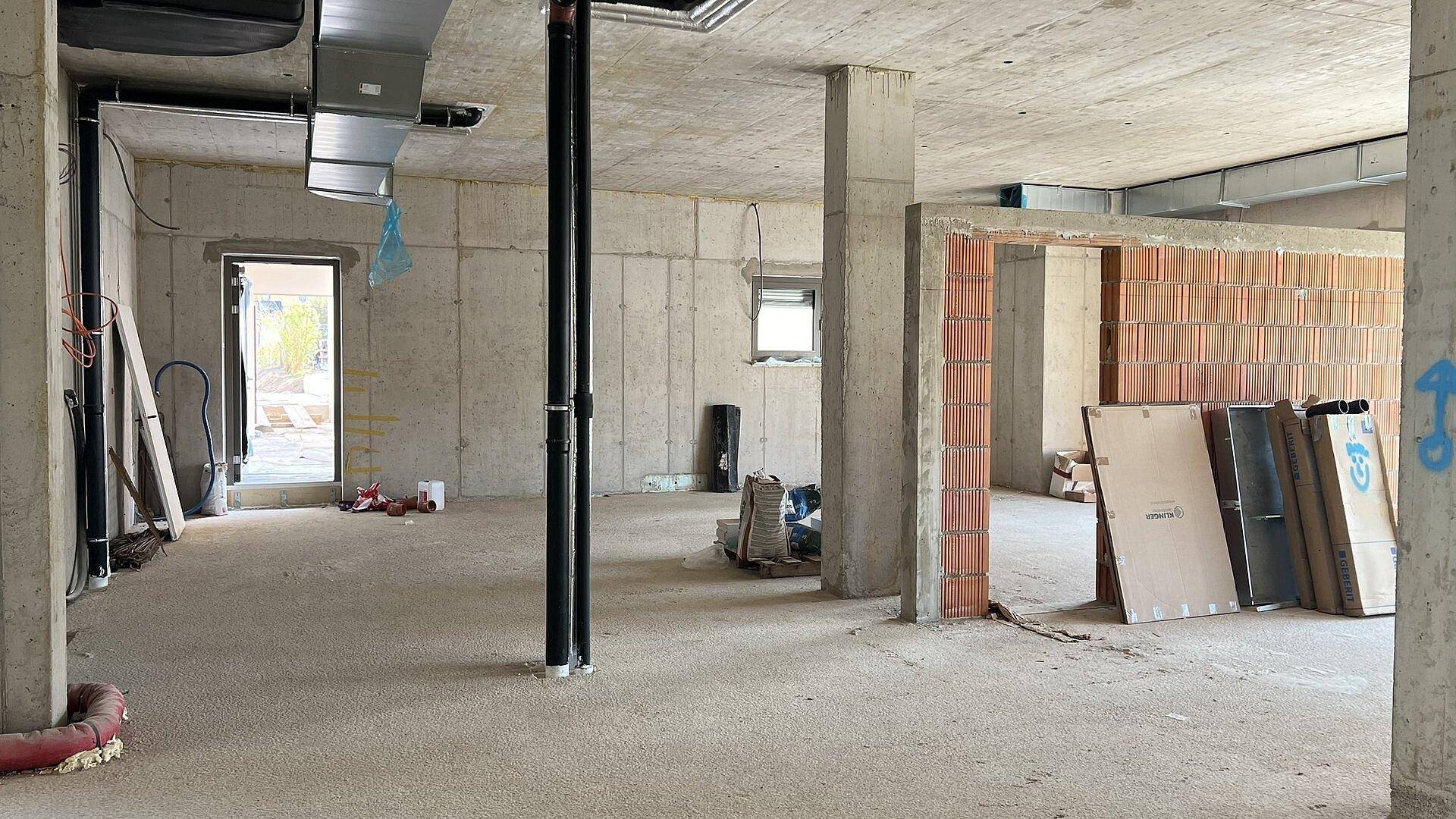 Großer Rohbau-Innenraum mit Betonwänden, freiliegenden Leitungen und Baustoffen, bereit für den Ausbau.