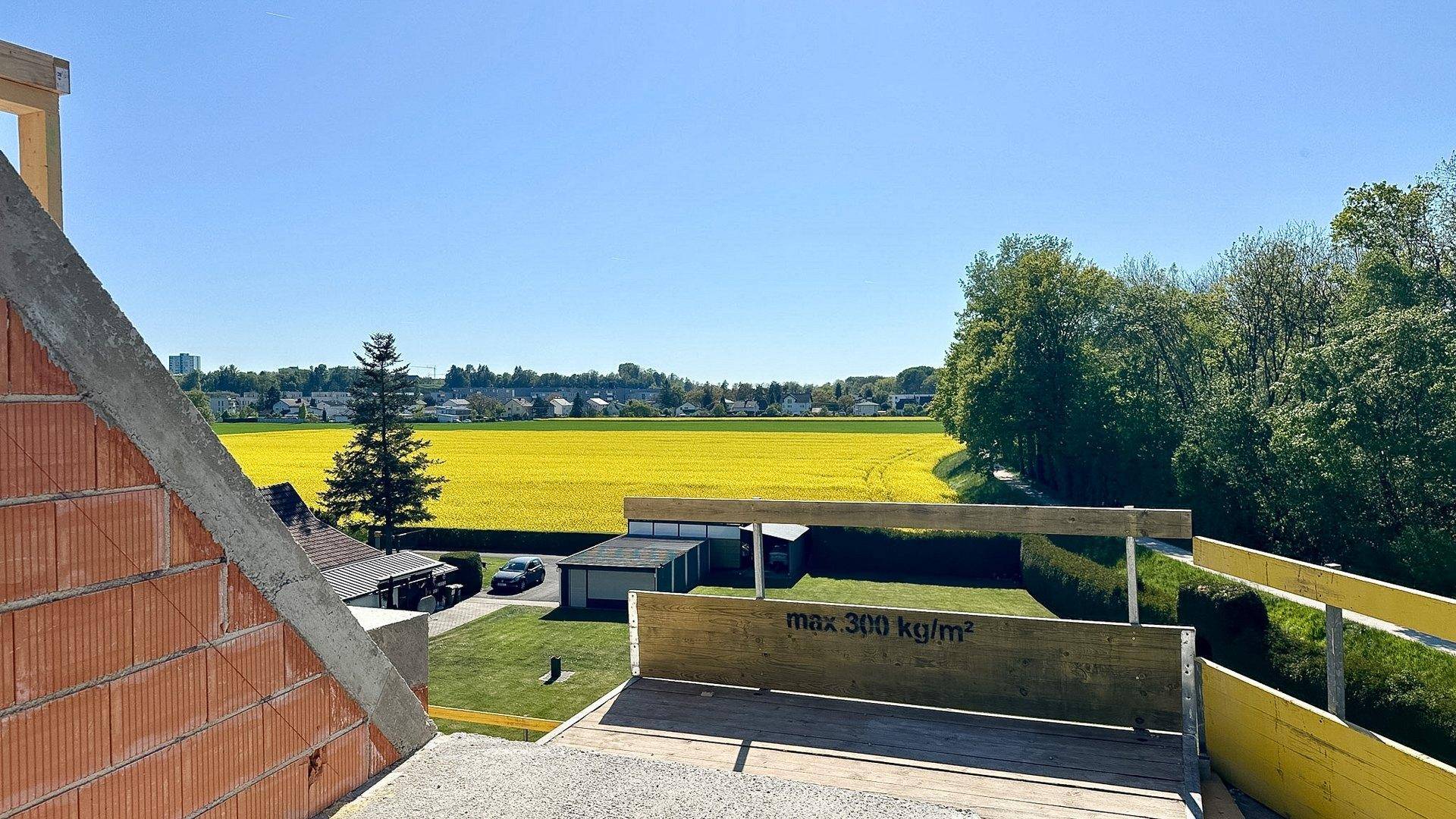 Blick von der Baustelle auf ein leuchtend gelbes Rapsfeld und die ländliche Umgebung.