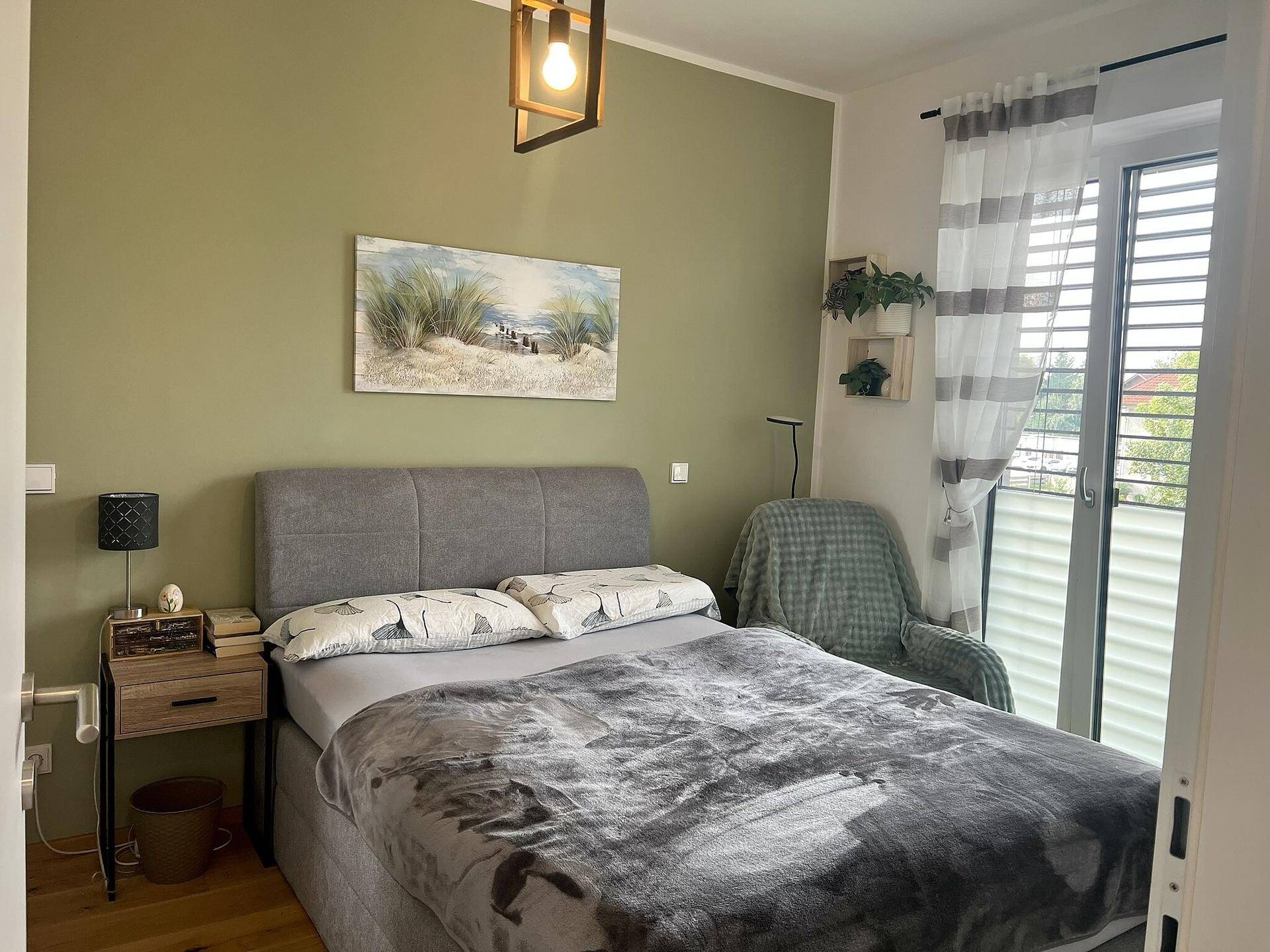 Komfortables Schlafzimmer mit Doppelbett, grünen Wänden und Zugang zum Balkon, hell und einladend.