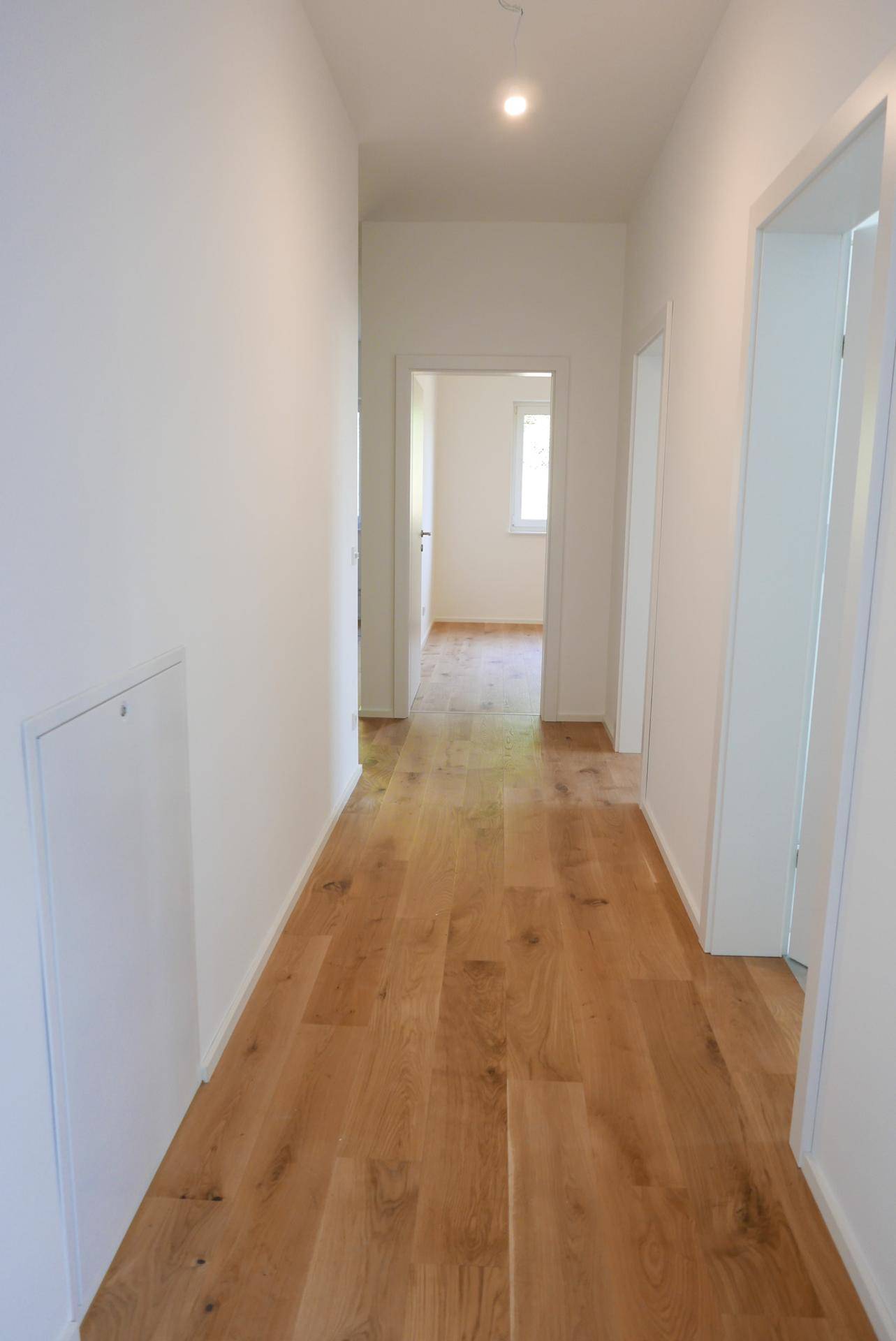 Heller Flur mit Holzboden und weißen Wänden, der zu weiteren Zimmern führt.