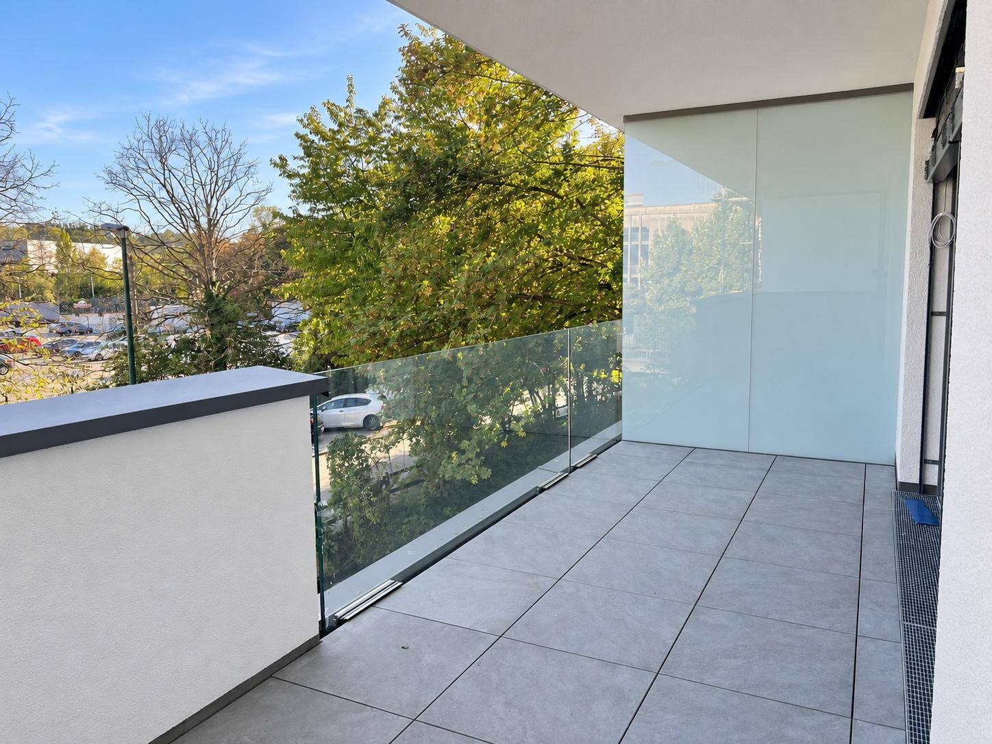 Moderner Balkon mit Fliesenboden, Glasgeländer und Blick auf die Umgebung.