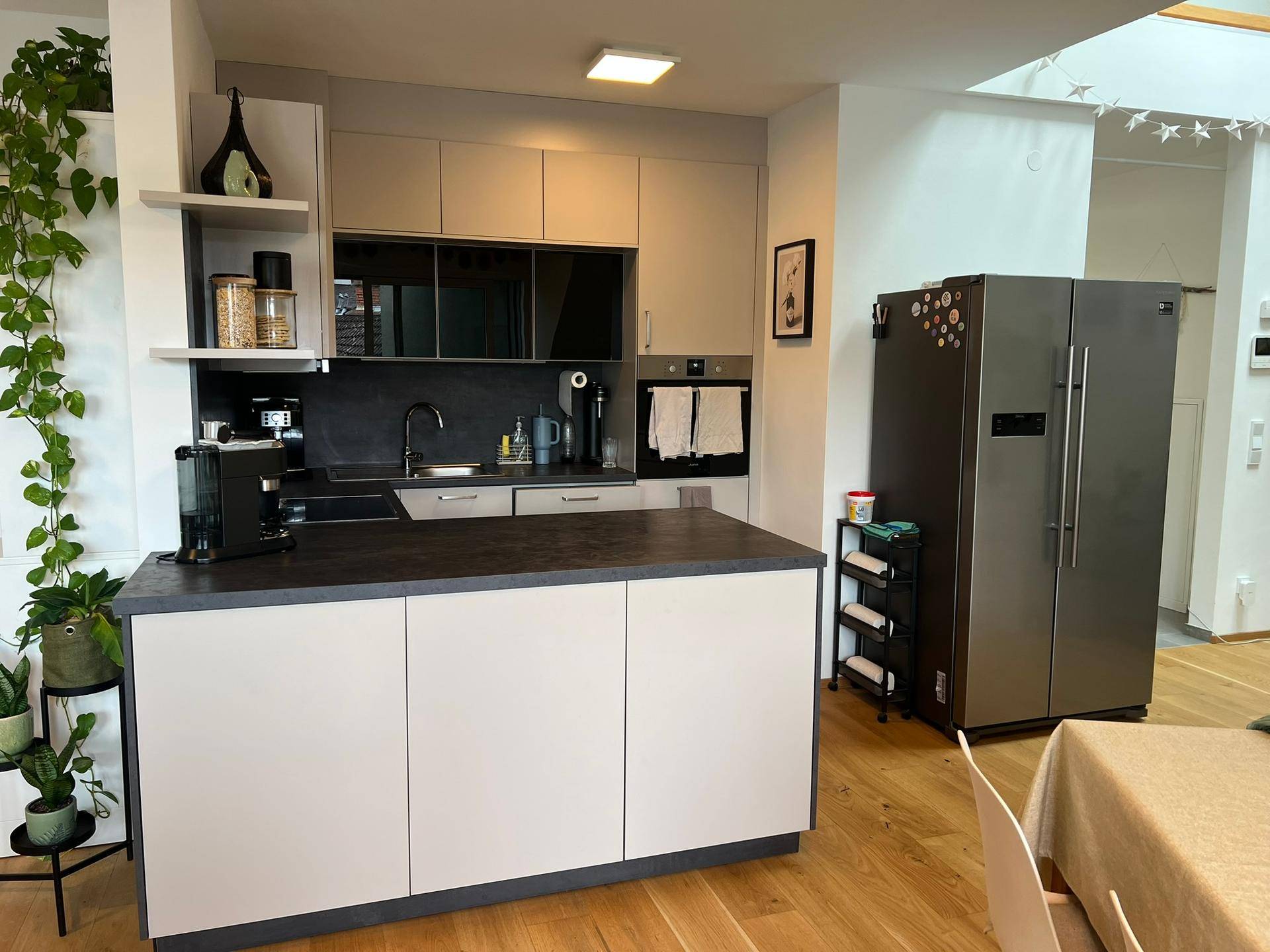 Moderne Küche mit Kücheninsel, integrierten Geräten und großem Kühlschrank, offen gestaltet.