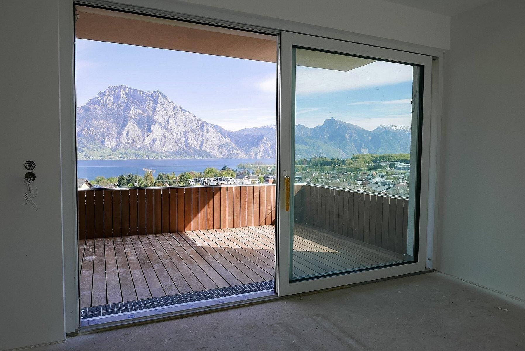 Heller Innenraum mit großen Schiebetüren, die Zugang zu einem Balkon mit Seeblick bieten.